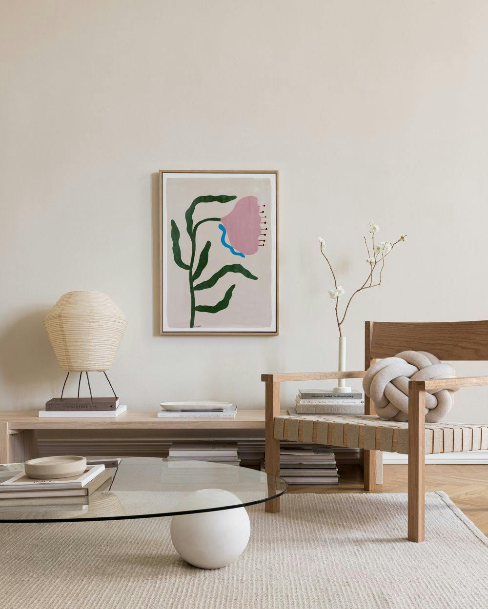 Lerretsbilde med rosa blomster og grønne blader, med blå detaljer, henger over en benk i en moderne stue.