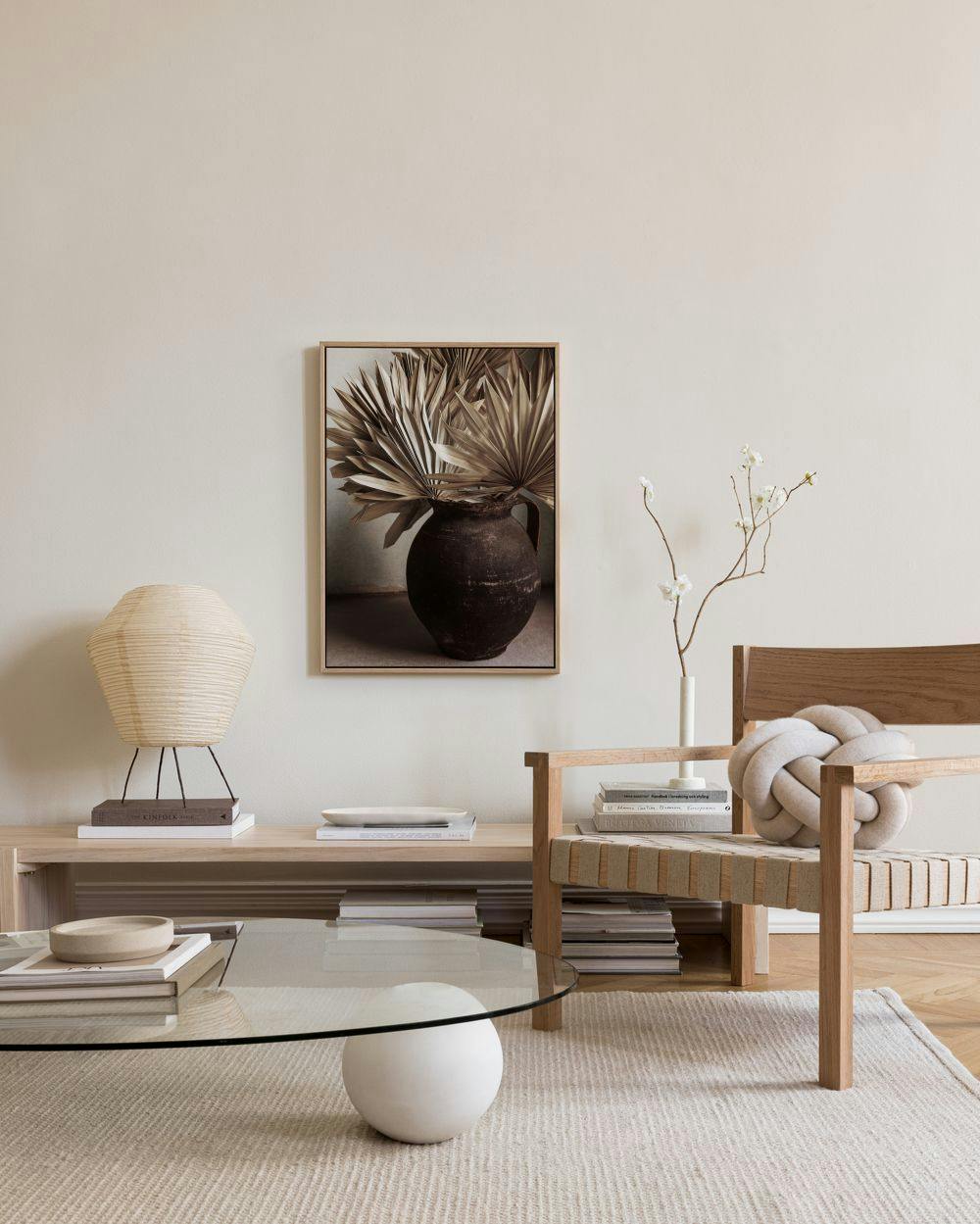 Lerretsbilde av en brun, rustikk vase med tørkede palmblader, henger i en lys stue over en benk.