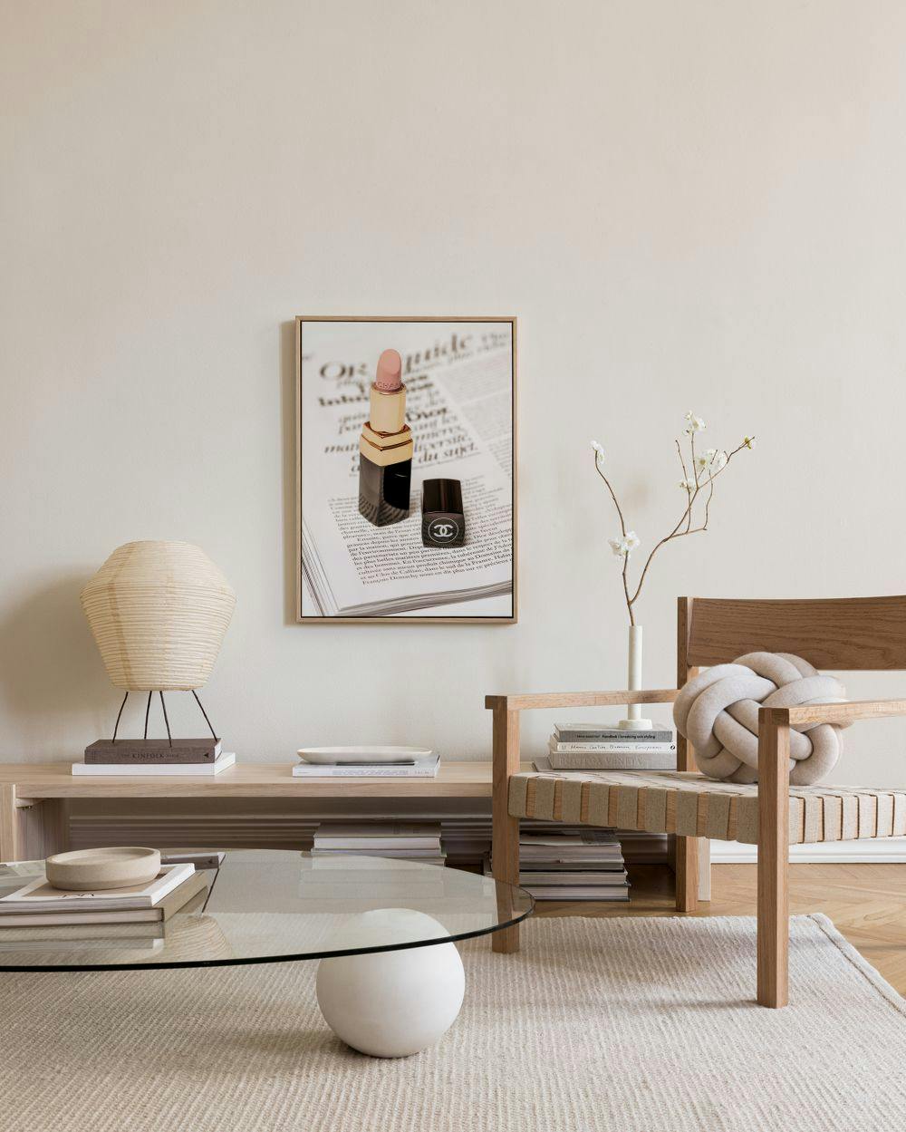 Lerretsbilde av leppestift og neglelakk på en avis, henger i en moderne stue over en benk.