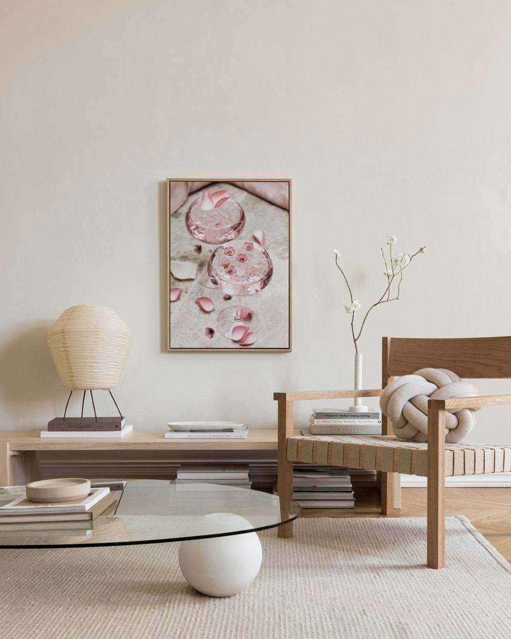A canvas print of two pink cocktails with rose petals, displayed in a modern living room above a wooden console table.