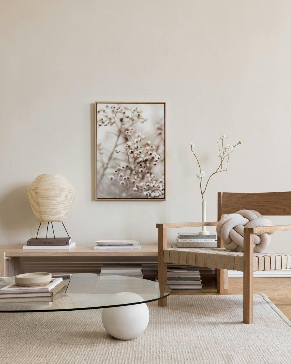 Naturlig lerretsbilde med detaljer av tørkede blomster og bær, henger over en benk i en lys stue.