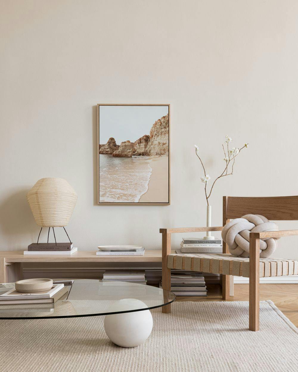 A canvas print of a sandy beach with crashing waves and large rock formations, displayed in a bright living room.