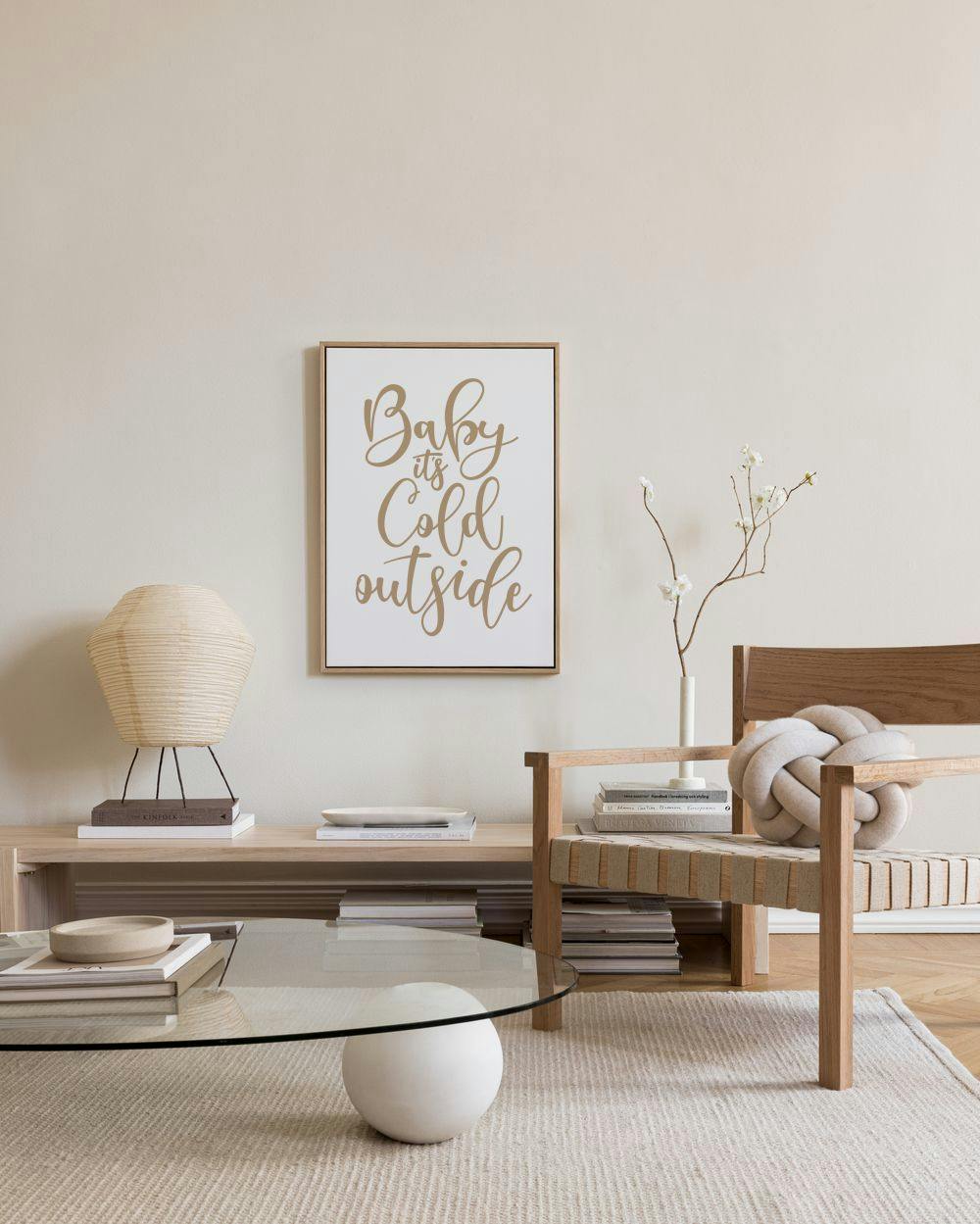 Toile Baby its Cold Outside en lettres dorées sur fond blanc, accrochée dans un salon moderne aux tons neutres.