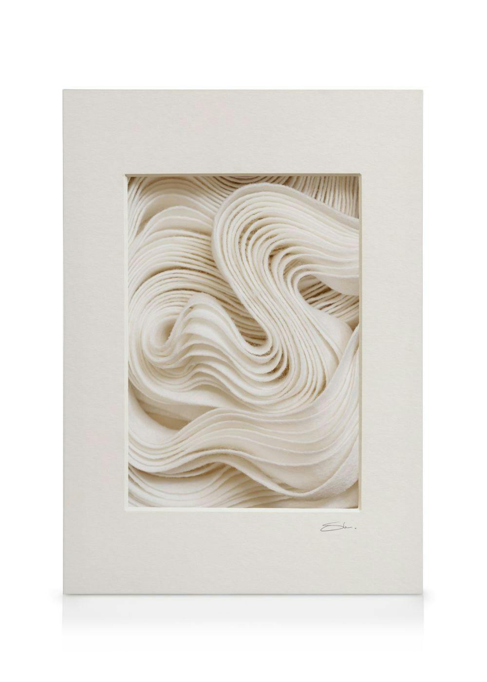 Lienzo con texturas onduladas blancas, enmarcado en beige con paspartú blanco, arte mural minimalista.