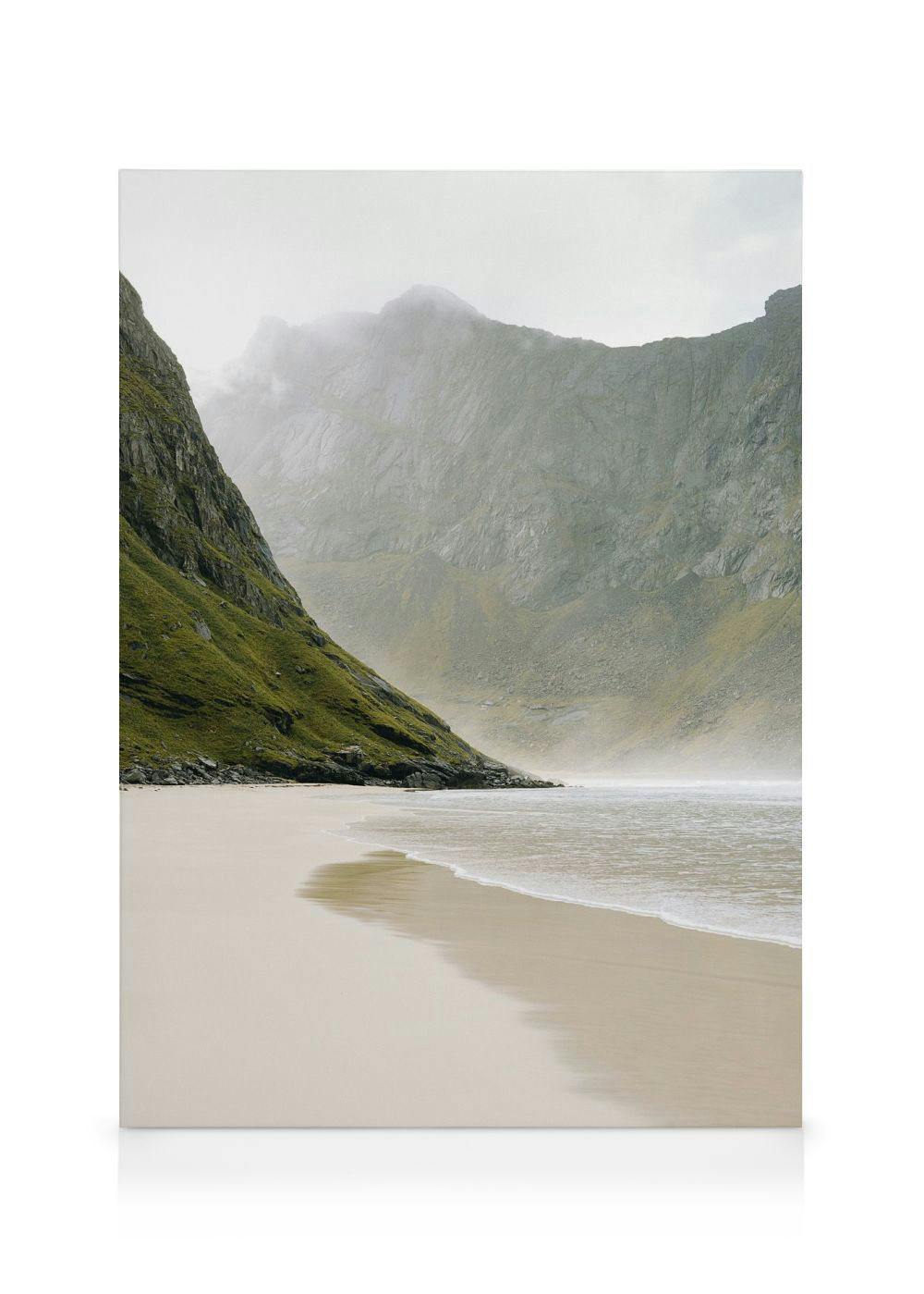 Fredelig lerretsbilde av strand, rolige bølger, grønne åser og grå fjell under lys, overskyet himmel.