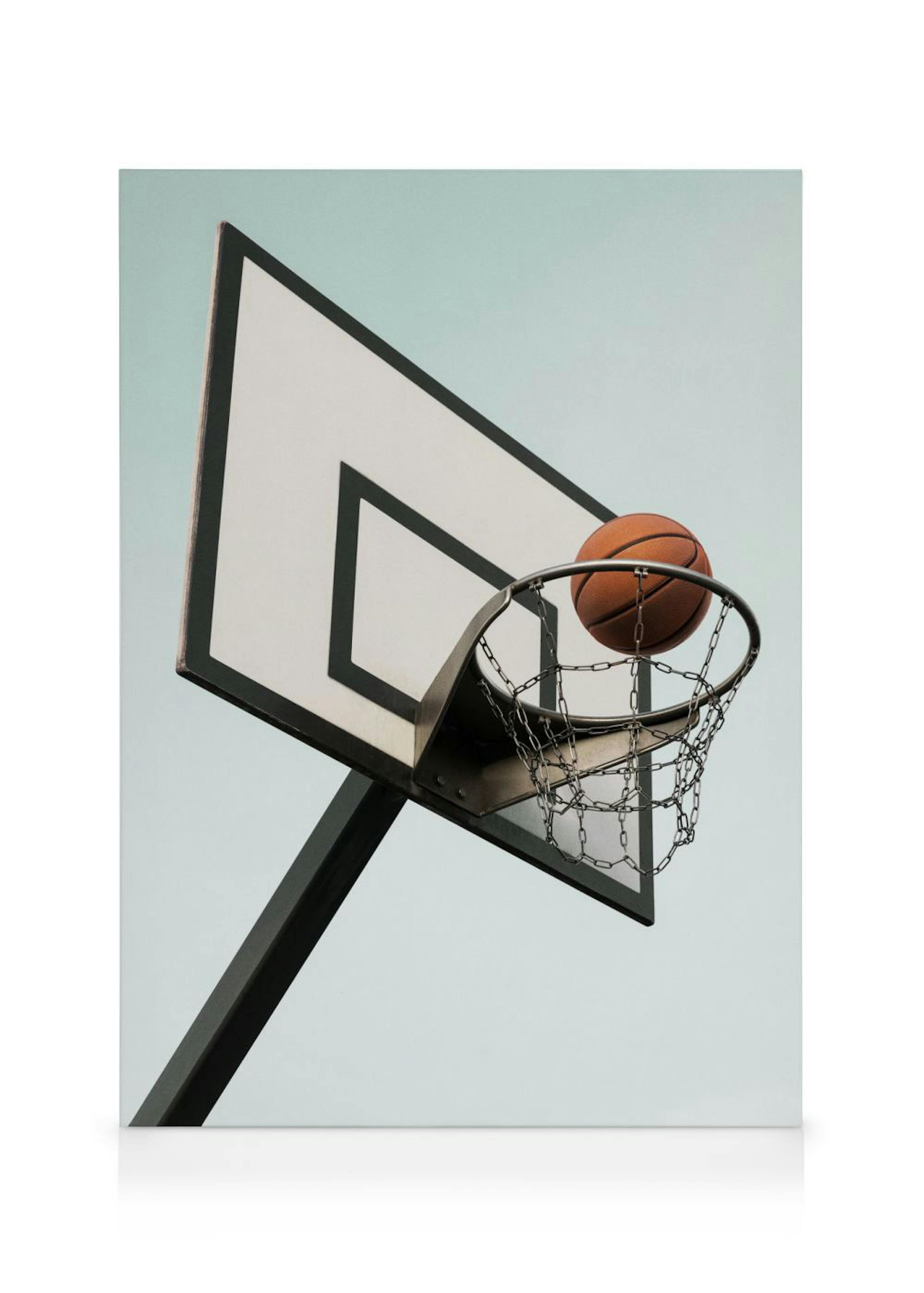 Basketball hoop with a ball falling through the net, captured from a low angle against a clear sky.