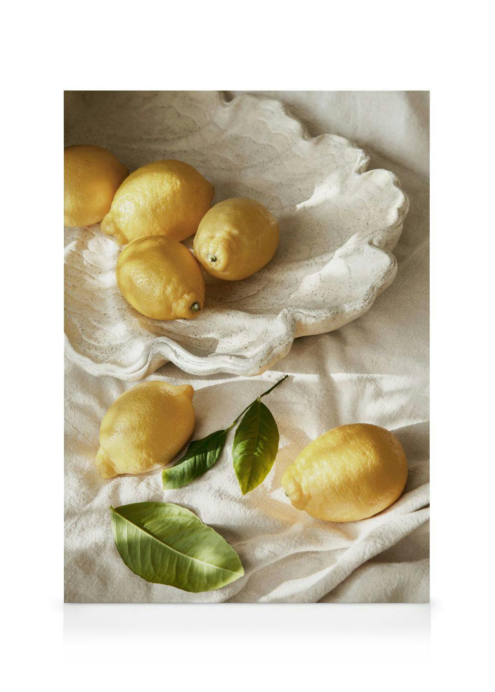 Leinwandbild mit Zitronen, einige auf einer strukturierten Schale, andere auf einem Leinentuch mit Blättern, im Sonnenlicht.