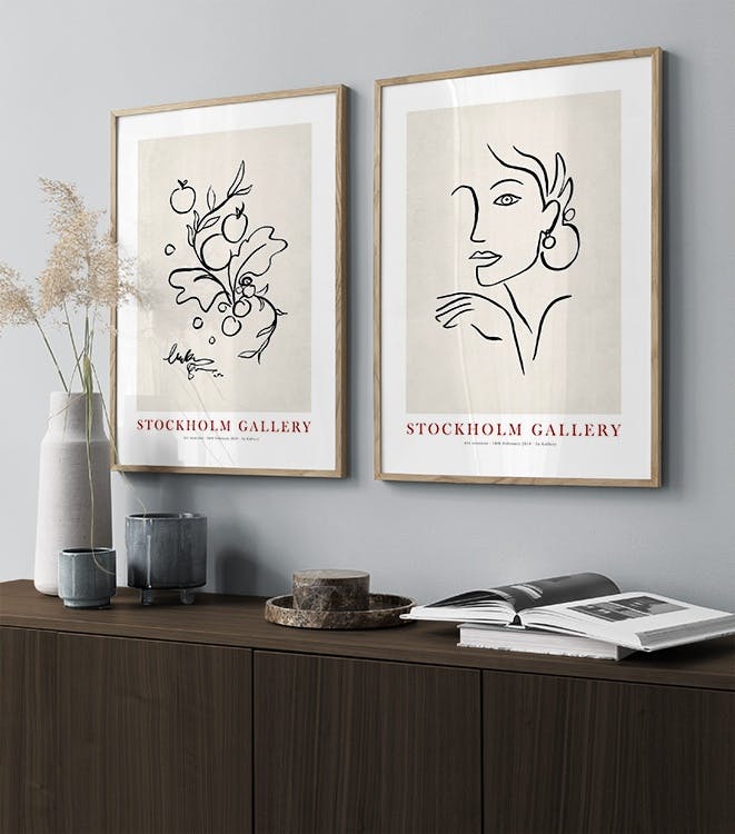 A gallery wall with two modern line art prints: one depicting stylized fruits and leaves, the other a womans profile.