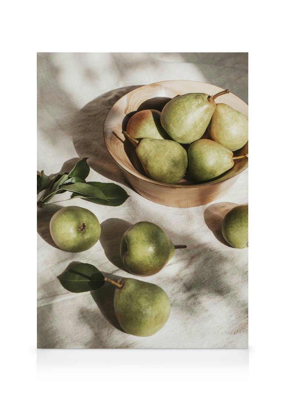 Sunlit green pears in a wooden bowl with scattered fruit and leaves on a beige cloth, creating a serene still life.