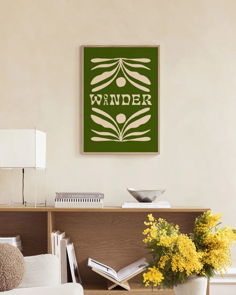 Poster met de tekst WANDER in beige, omgeven door abstracte bladvormen op een groene achtergrond, hangend boven een houten dress