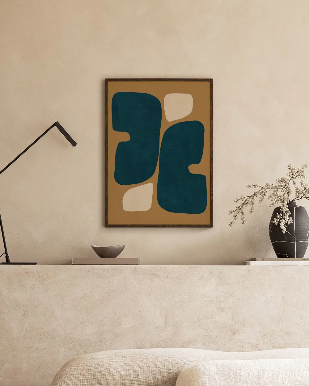 Poster mit organischen Formen in Petrol und Beige auf braunem Hintergrund, in einem modernen Raum über einem Sofa.