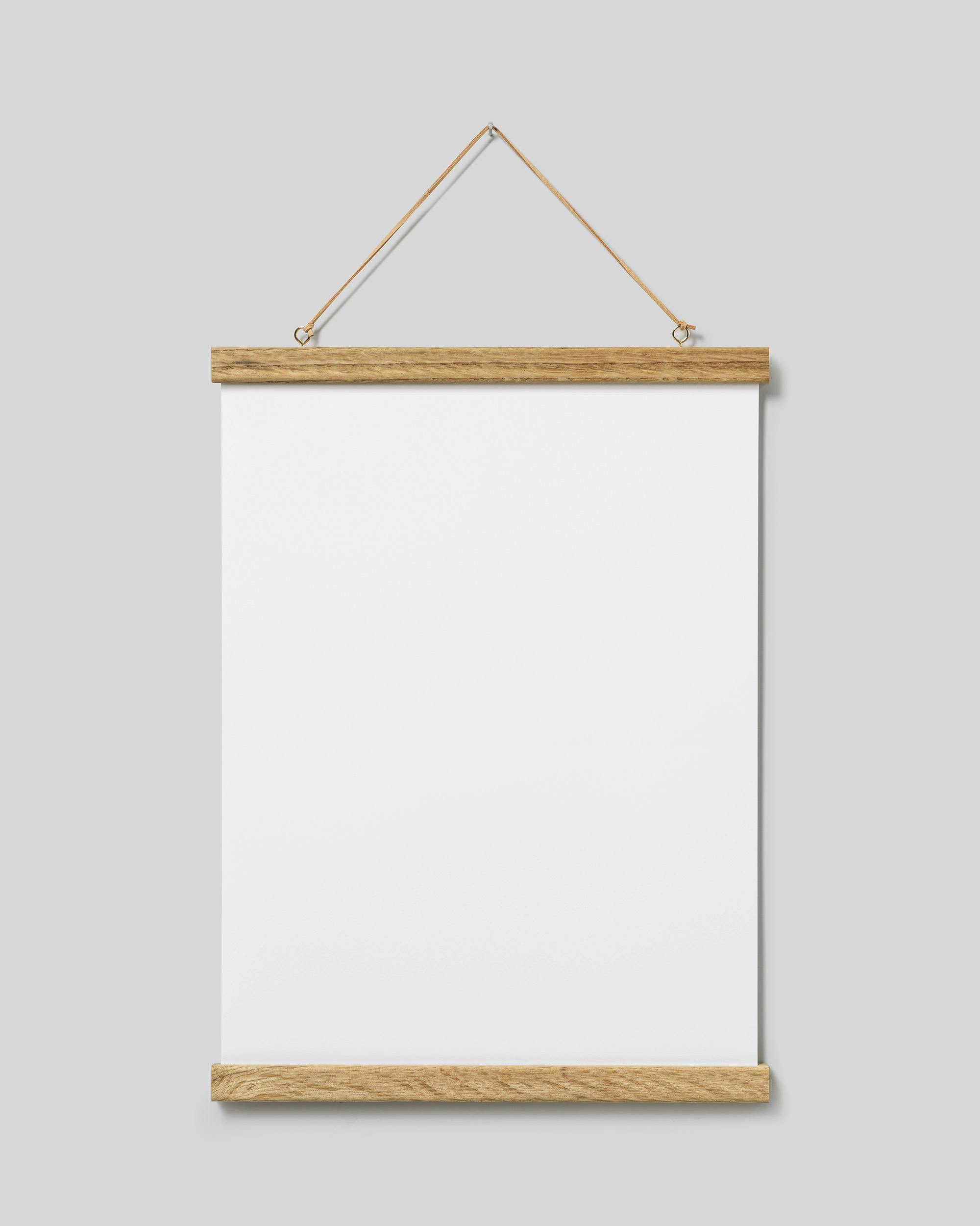 Eiken posterhanger met magneetbevestiging en suède koord, hangt aan de muur met een wit vel papier erin.