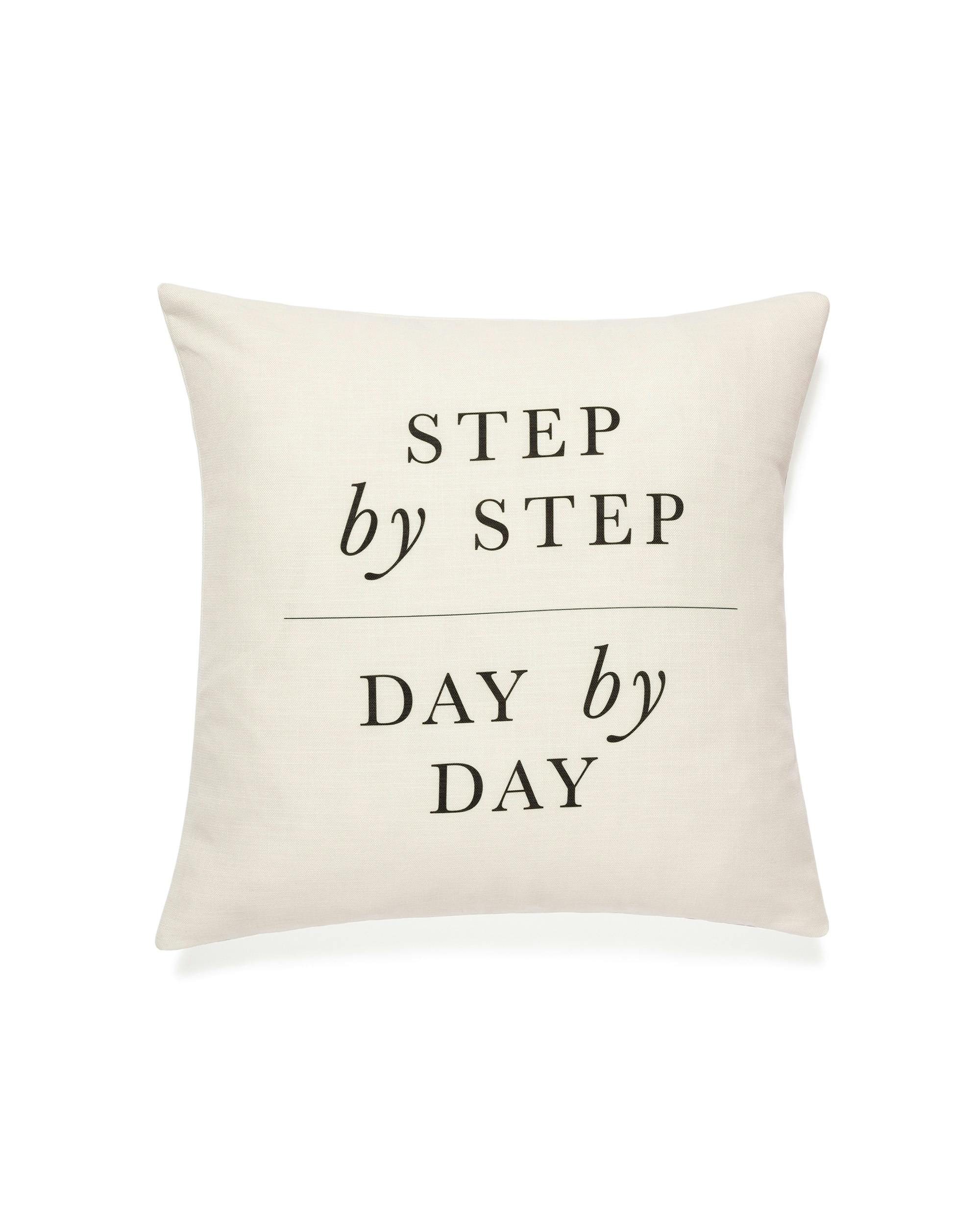 Funda de cojín blanca con el texto Step by Step Day by Day en tipografía negra.