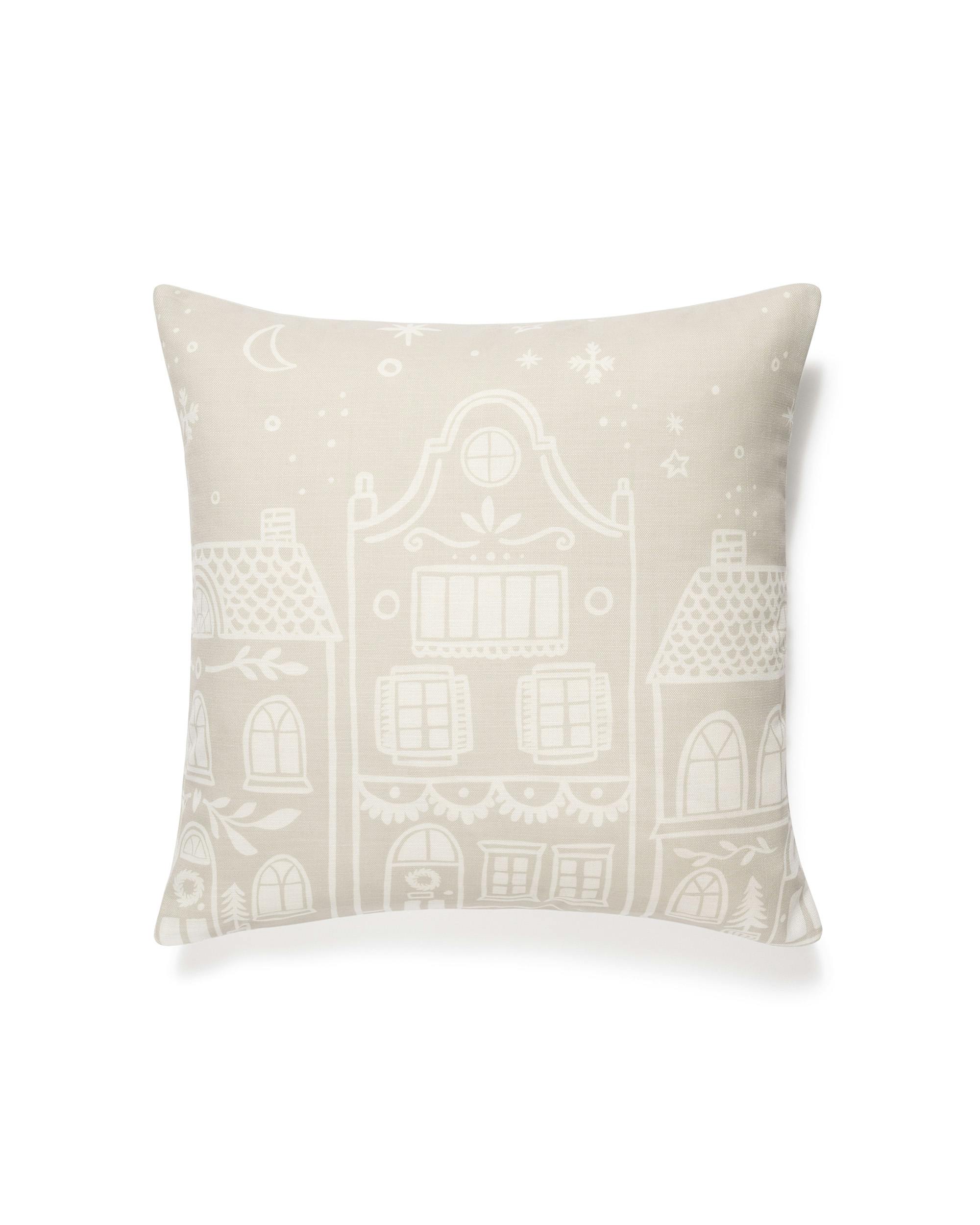 Housse de coussin beige avec typographie blanche représentant une ville enneigée sous la lune et les étoiles, avec des flocons d