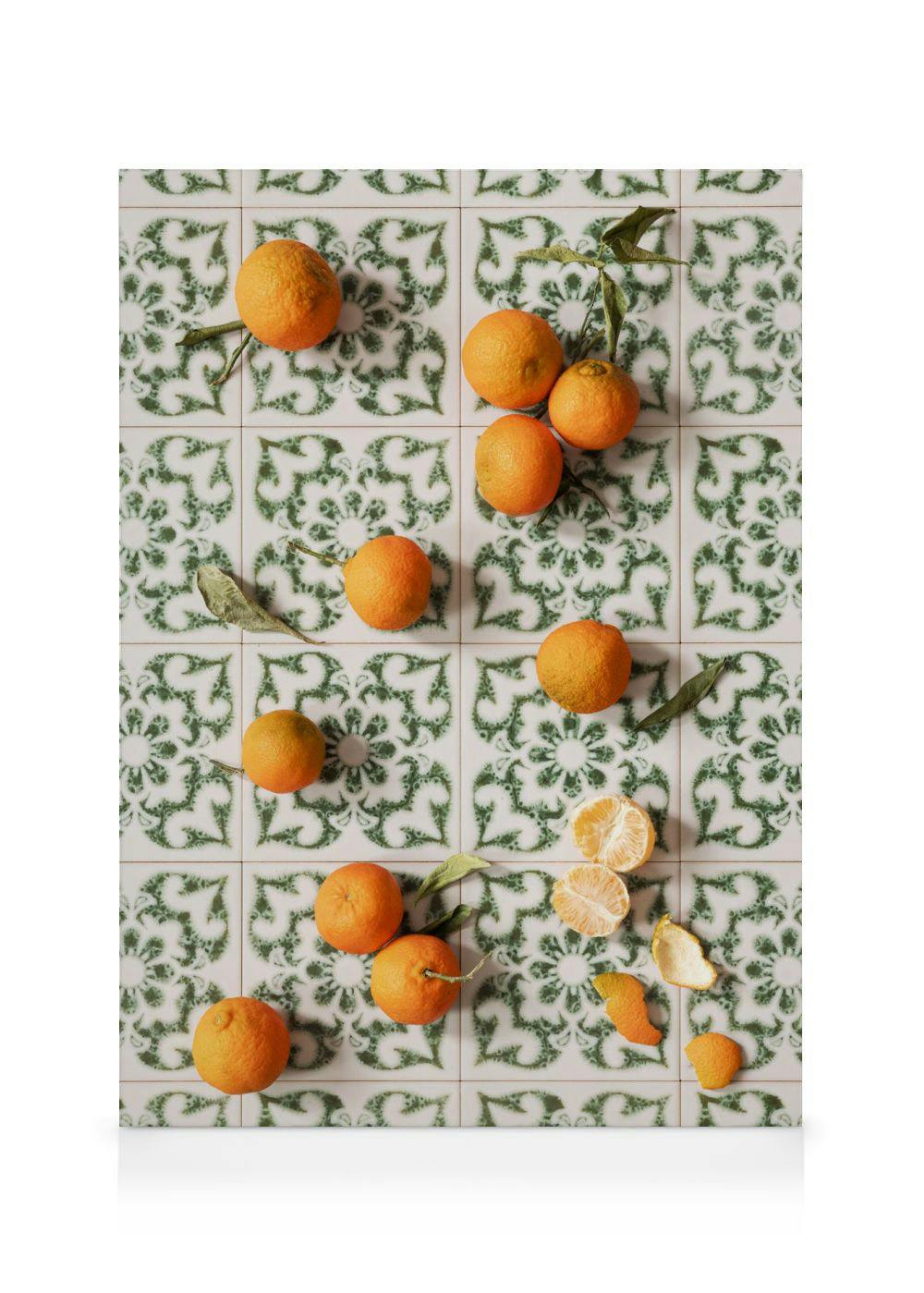 A canvas print of tangerines with leaves and peels on white tiles with a green patterned design.