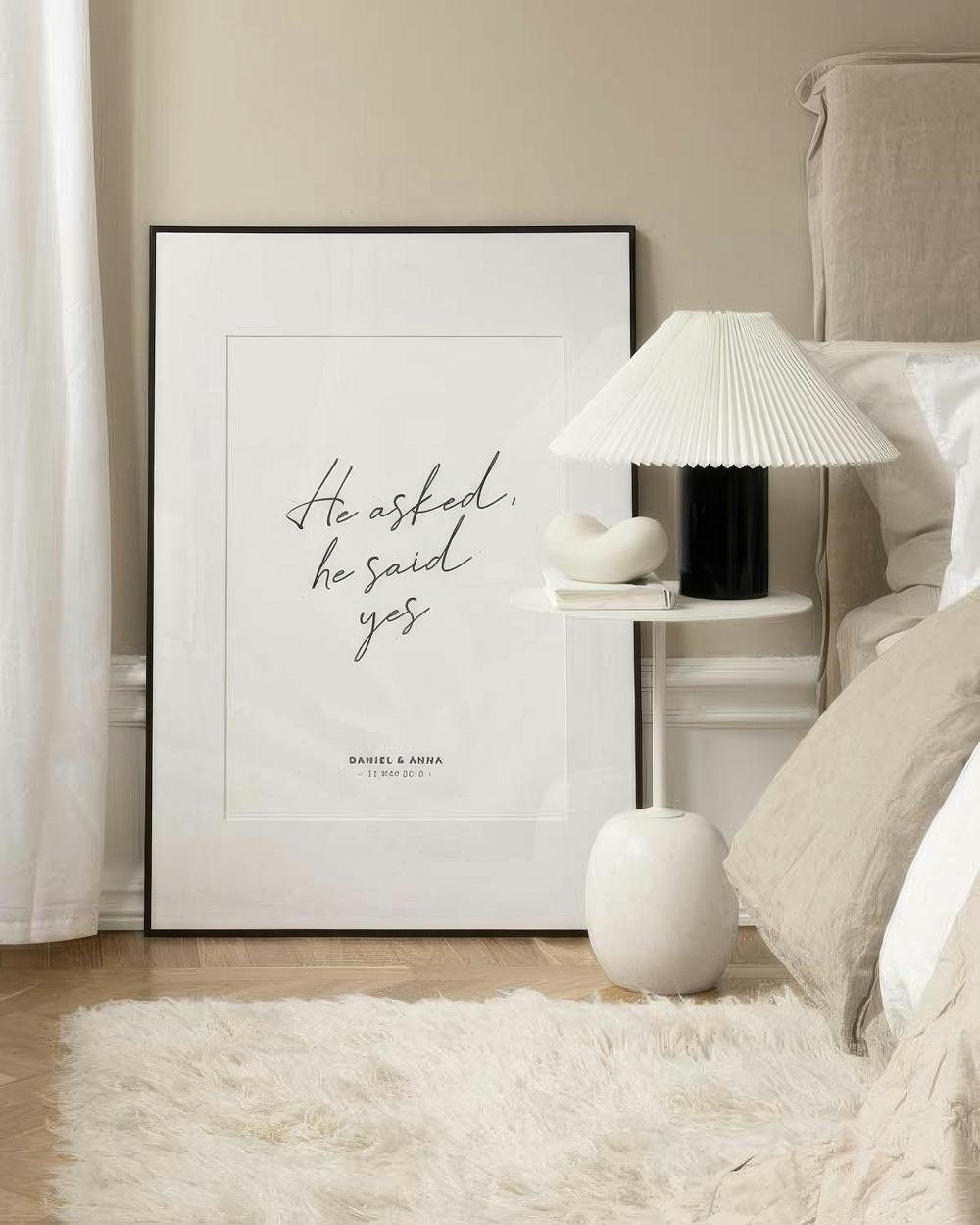 A personalised print with black script text He asked, he said yes and names/date below, leaning against a bedroom wall.