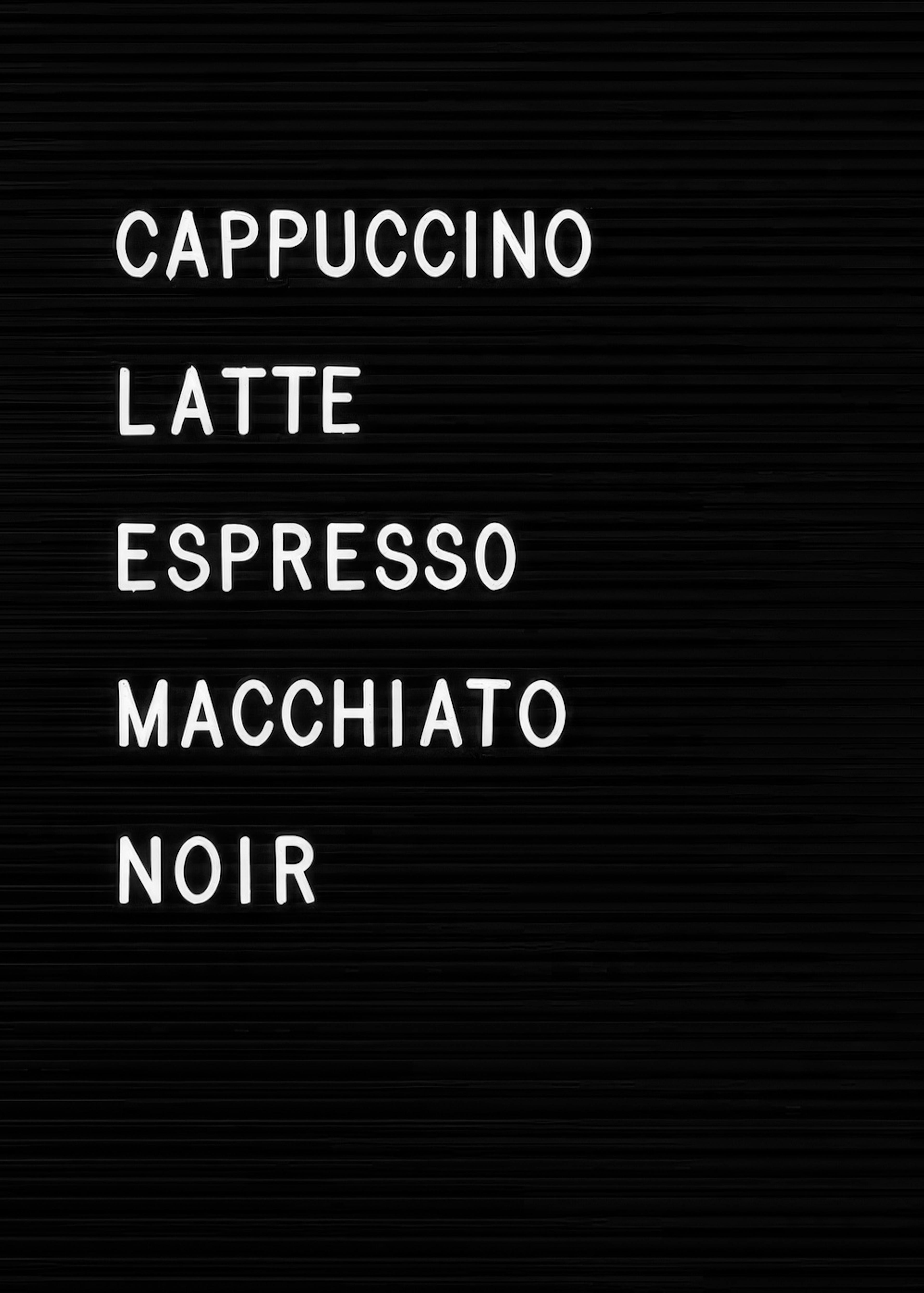 A print of a black letter board with white plastic letters spelling out CAPPUCCINO, LATTE, and ESPRESSO.