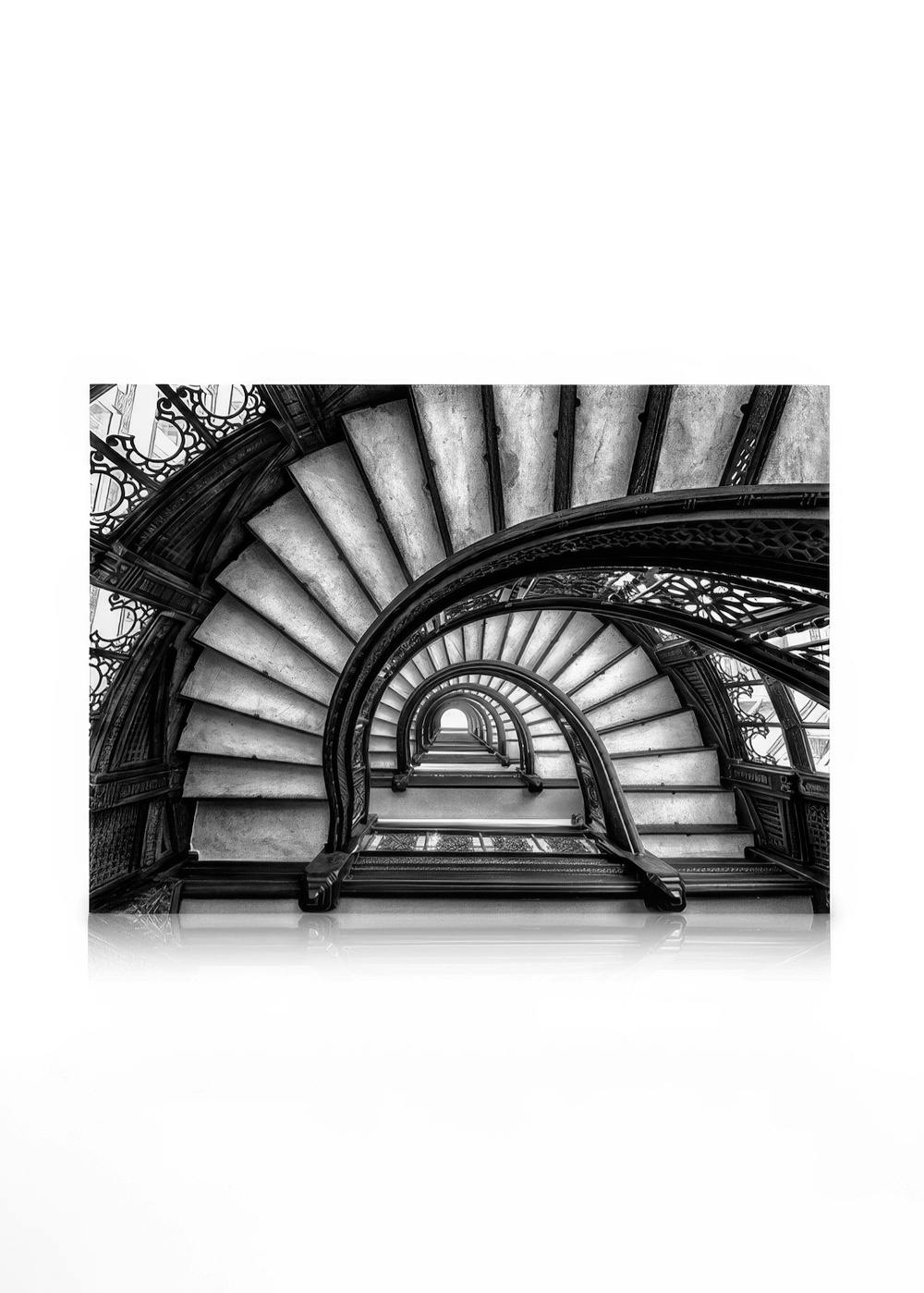 Sort/hvid lærredstryk af en snoet trappe med detaljeret gelænder og marmortrin, set nedefra. Arkitektur lærred.