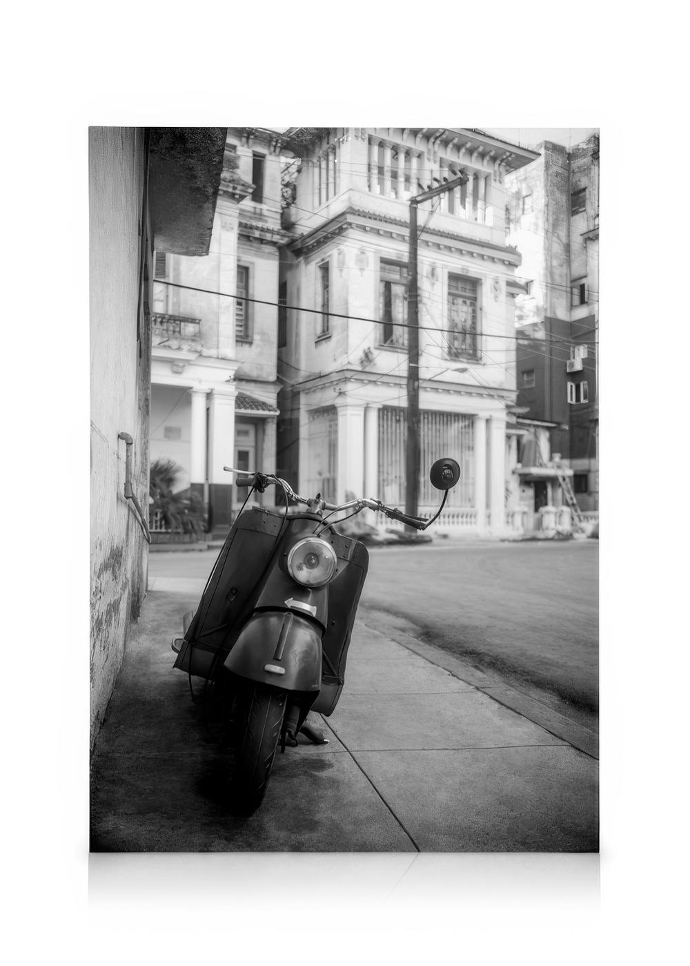 Toile noir et blanc dun scooter vintage garé sur un trottoir avec des bâtiments historiques de Cuba en arrière-plan