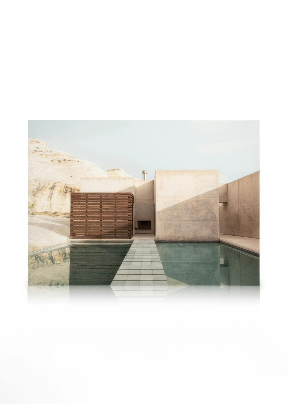Photo of a calm, minimalist pool with clear blue water, beige concrete walls, and a brown wooden structure.