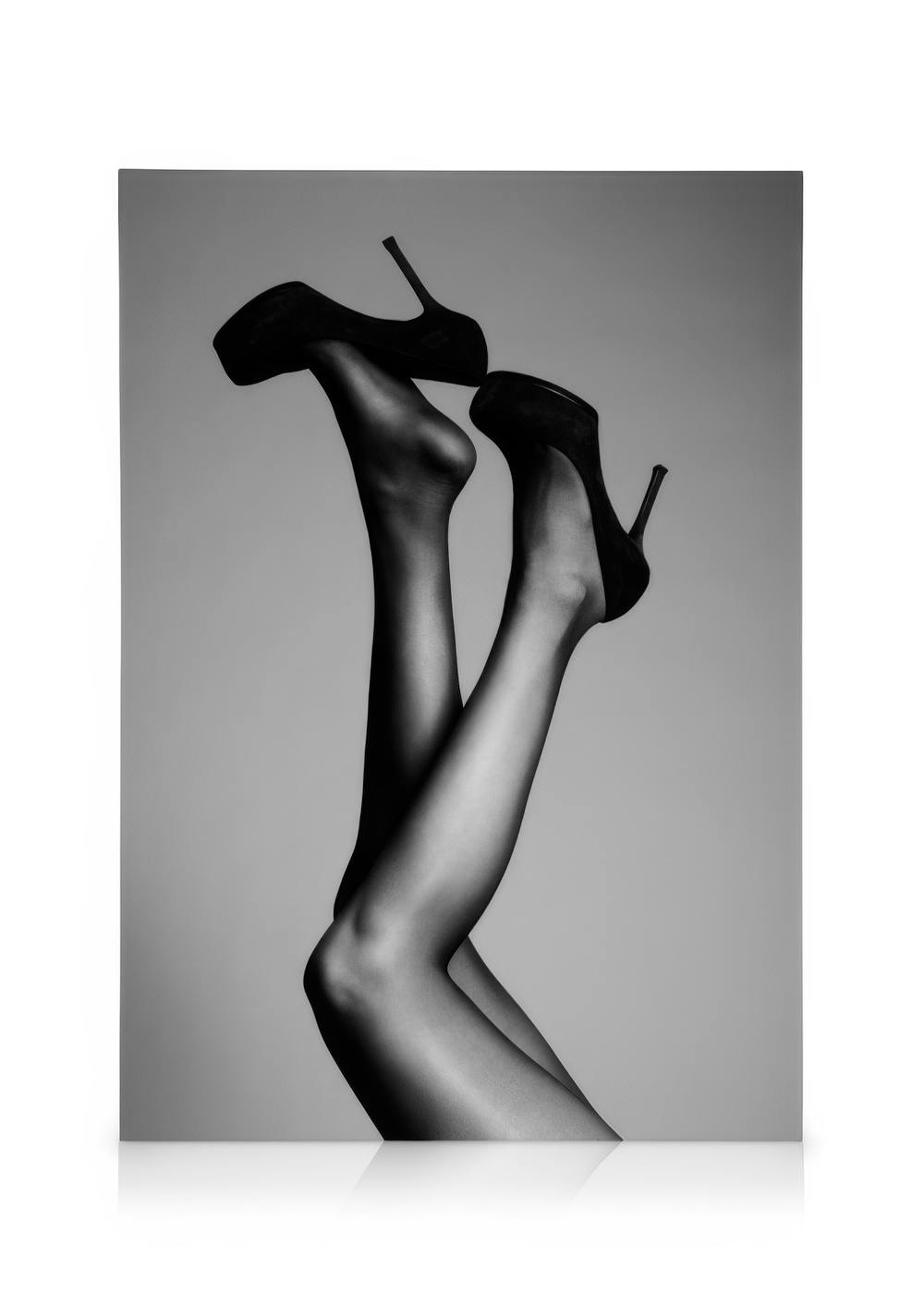 Schwarz-weißes Leinwandbild mit Frauenbeinen in schwarzen Strümpfen und High Heels, die elegant in die Luft ragen.