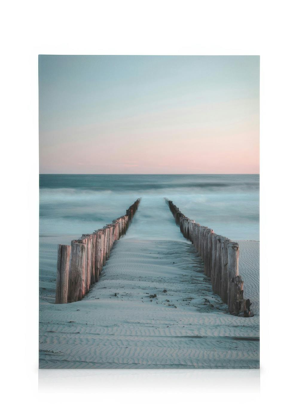 Towards the Sea canvas print featuring wooden groynes on a sandy beach at sunset, with a soft pink and blue sky.