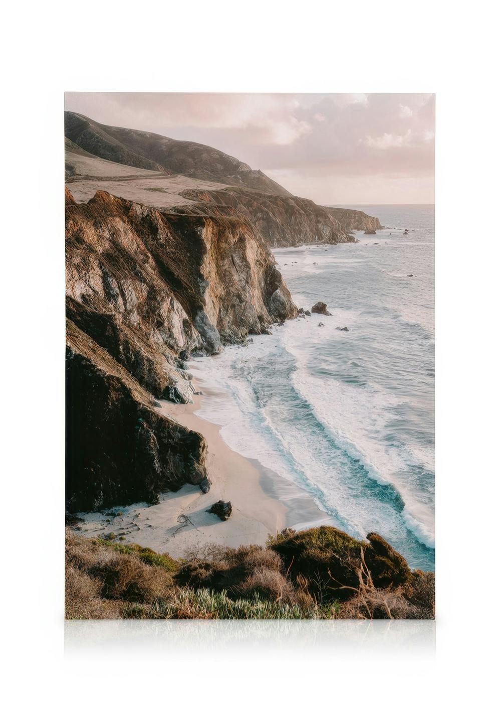 Quadro em tela da Costa de Big Sur com penhascos rochosos, praia arenosa e ondas oceânicas ao pôr do sol.