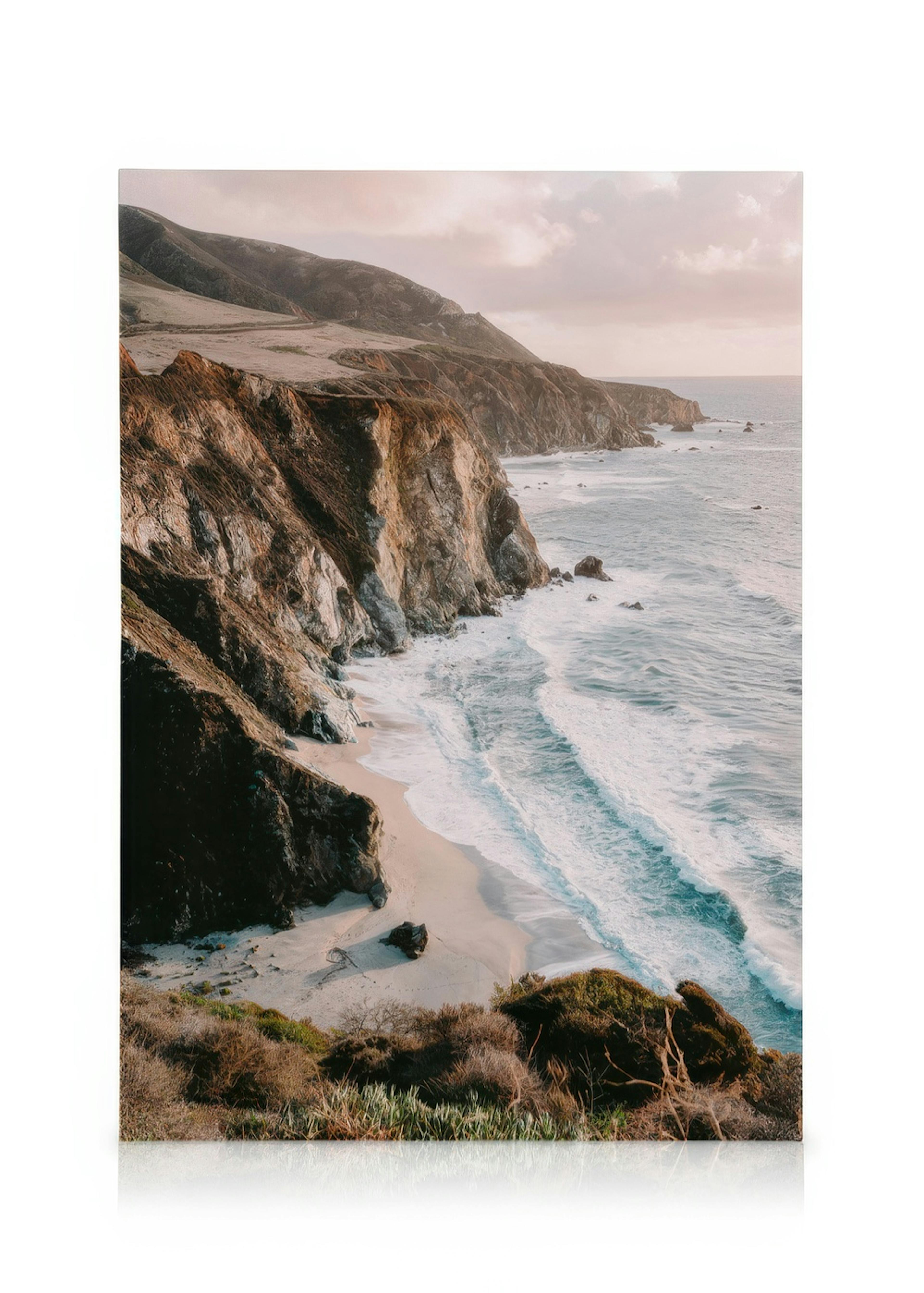 Toile de la côte de Big Sur avec des falaises, une plage de sable et des vagues océaniques sous un ciel nuageux.