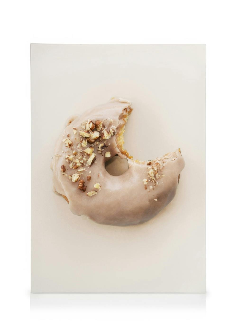 Bitten donut with light brown icing and chopped nuts on a neutral background, food art canvas