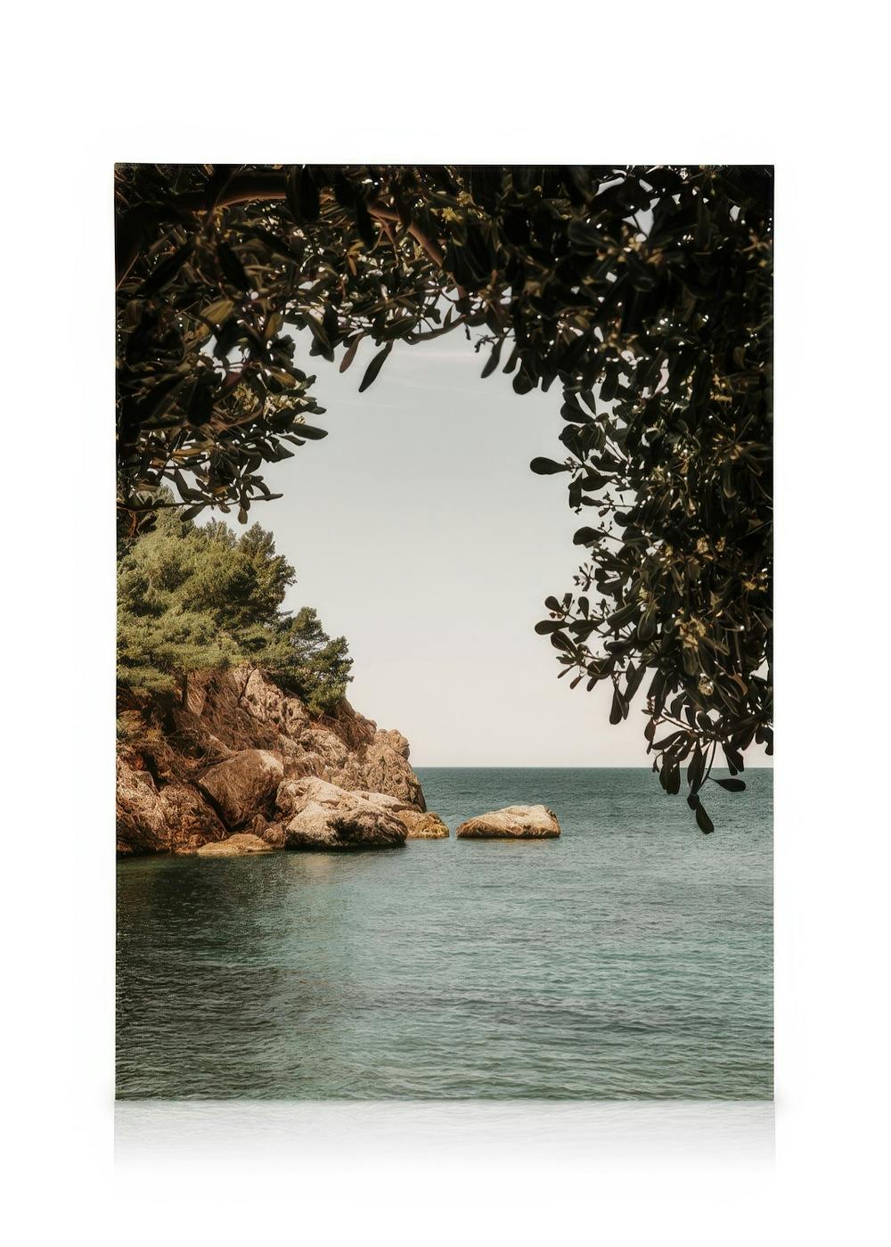 Organic Arch Canvas print of a serene sea framed by rocks and trees, blue-green water under a pale blue sky.