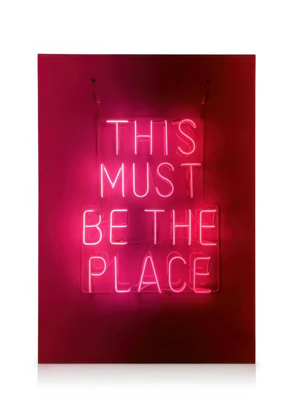 Neon sign canvas print with This Must Be The Place in bright pink light on dark pink wall, modern pop art.