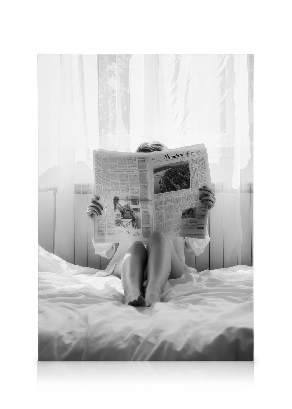 Mustavalkoinen kanvaasi naisesta lukemassa sanomalehteä sängyssä, valoisa aamu. Sisustuskuva.
