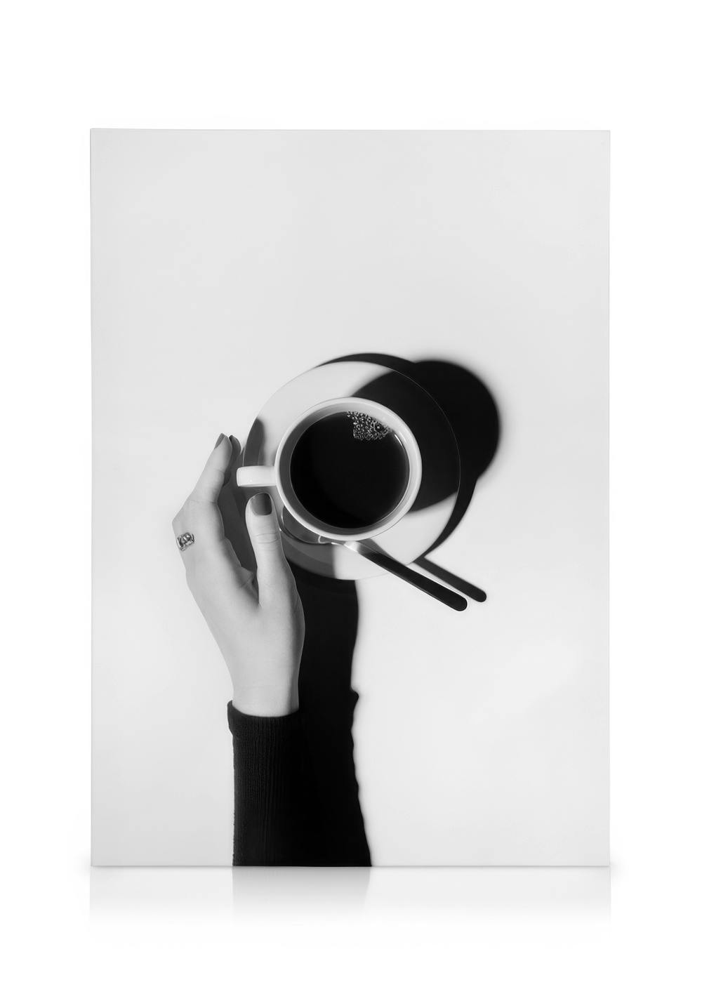 Black and white coffee canvas print with hand holding a cup, saucer, and spoon, perfect for dining room or kitchen art.
