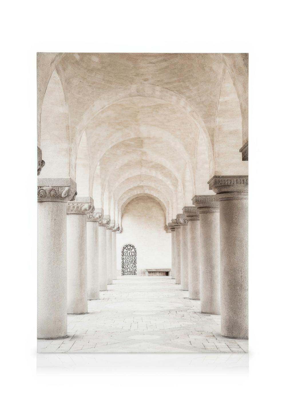 Fotografi af en lang korridor i beige stenbygning med søjler og hvælvede lofter samt metalgitter for enden.