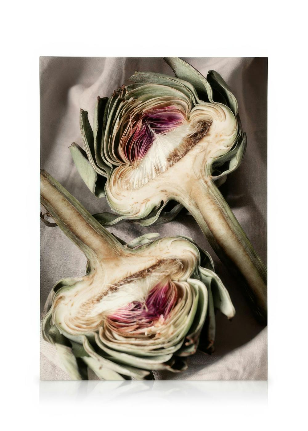 Dos alcachofas partidas por la mitad con centros morados y blancos, sobre tela gris. Arte de cocina.