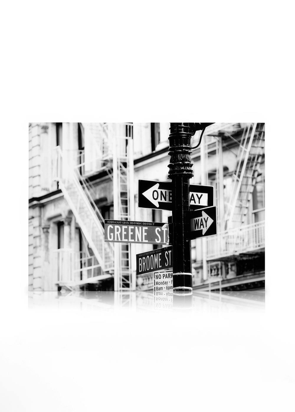 Svartvit fotografering av gatuskyltar i New York, inklusive One Way, Greene St och Broome St, med byggnader i bakgrunden.