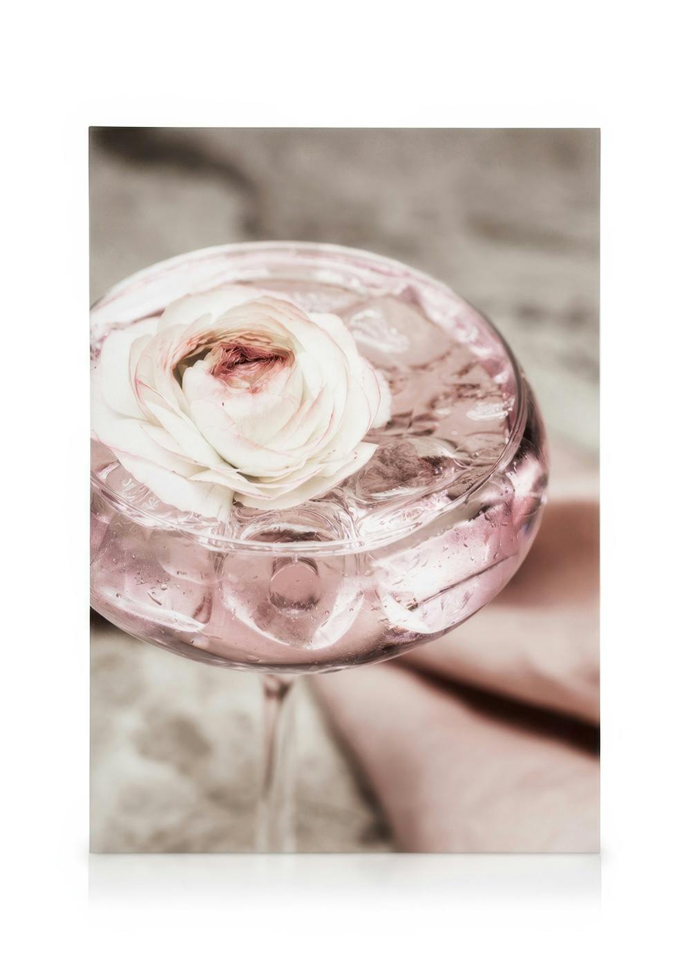 Ett glas med rosa cocktail och isbitar, toppat med en vit och rosa blomma.