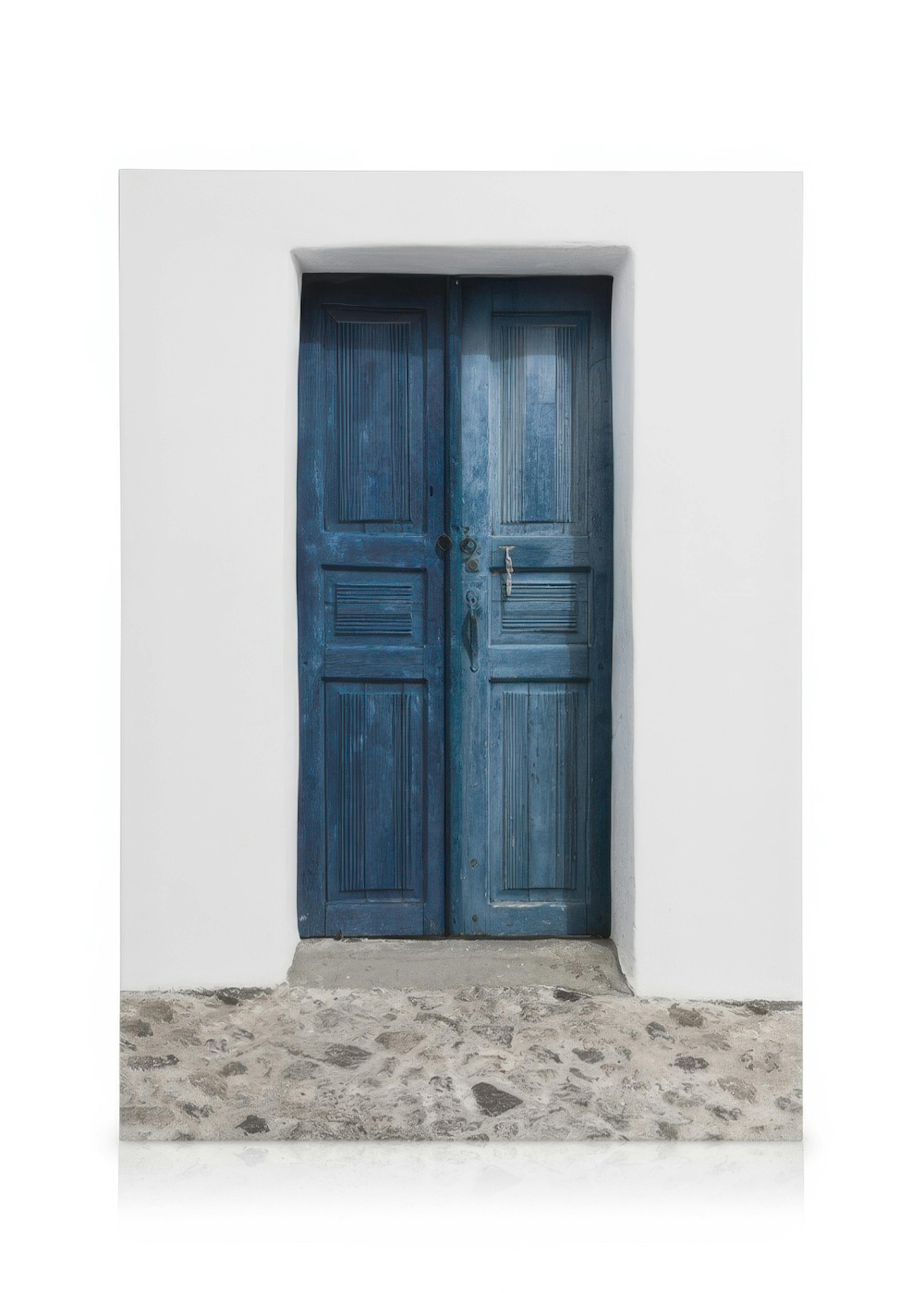 Lerretsbilde av en værslitt blå tredør med dekorative riller, mot en hvit vegg og grå brostein. Oia, Santorini inspirert.