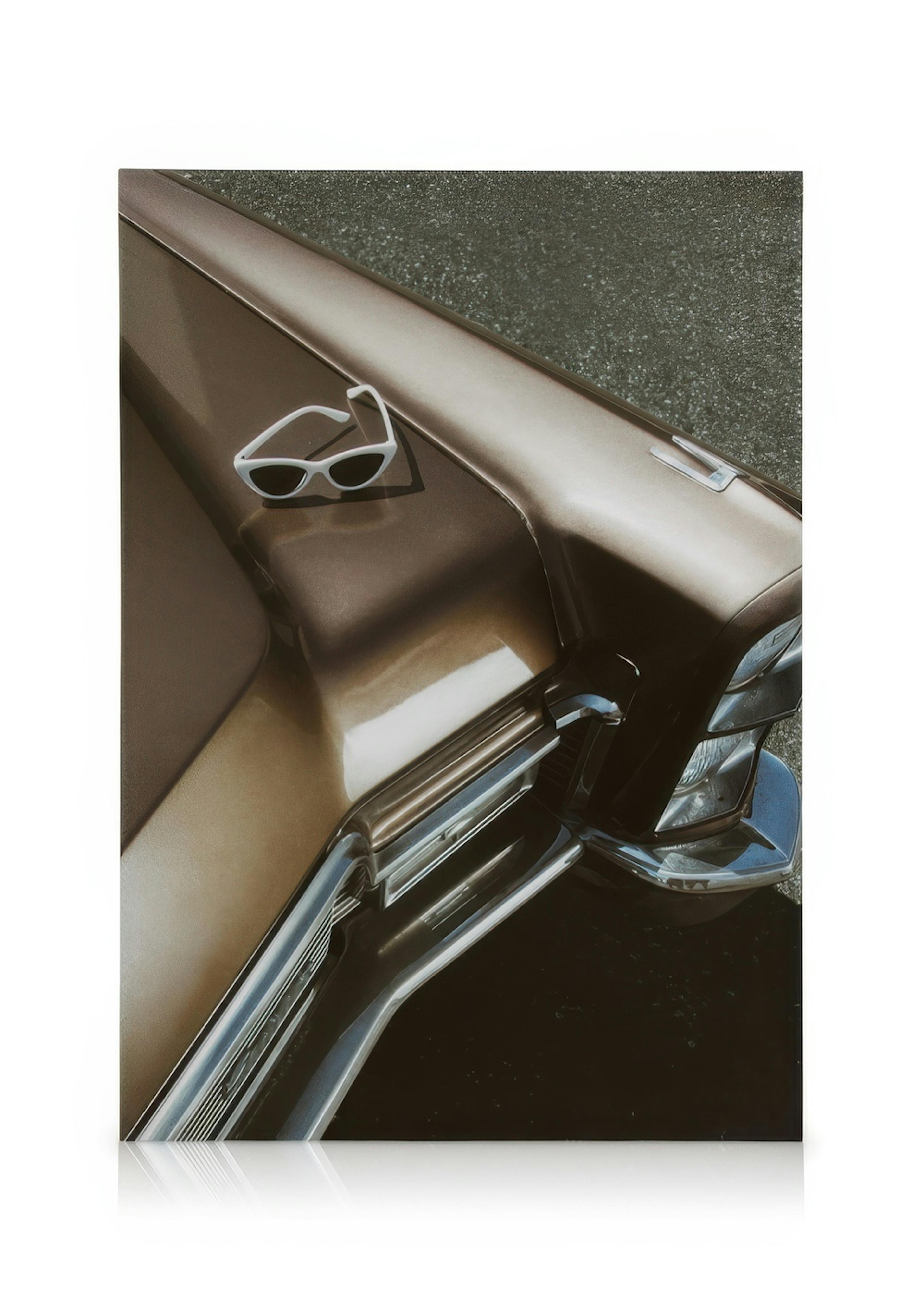 White sunglasses resting on a shiny brown Cadillac car hood with reflective chrome car parts.