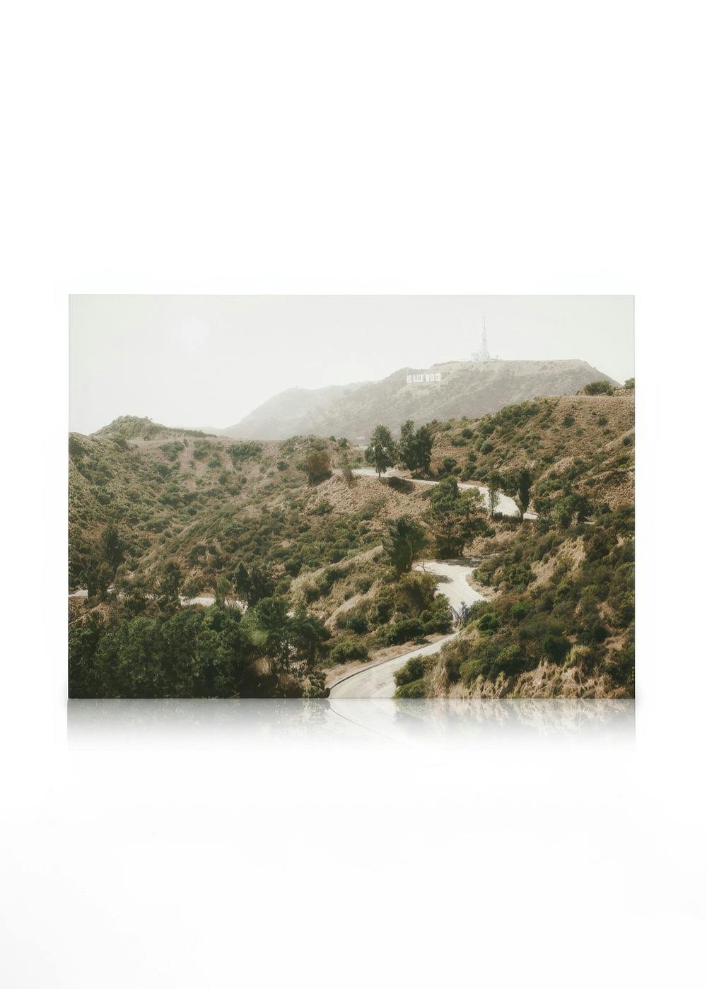 Lienzo de carretera serpenteante a través de colinas verdes, con letras de Hollywood en la distancia y un efecto granulado.