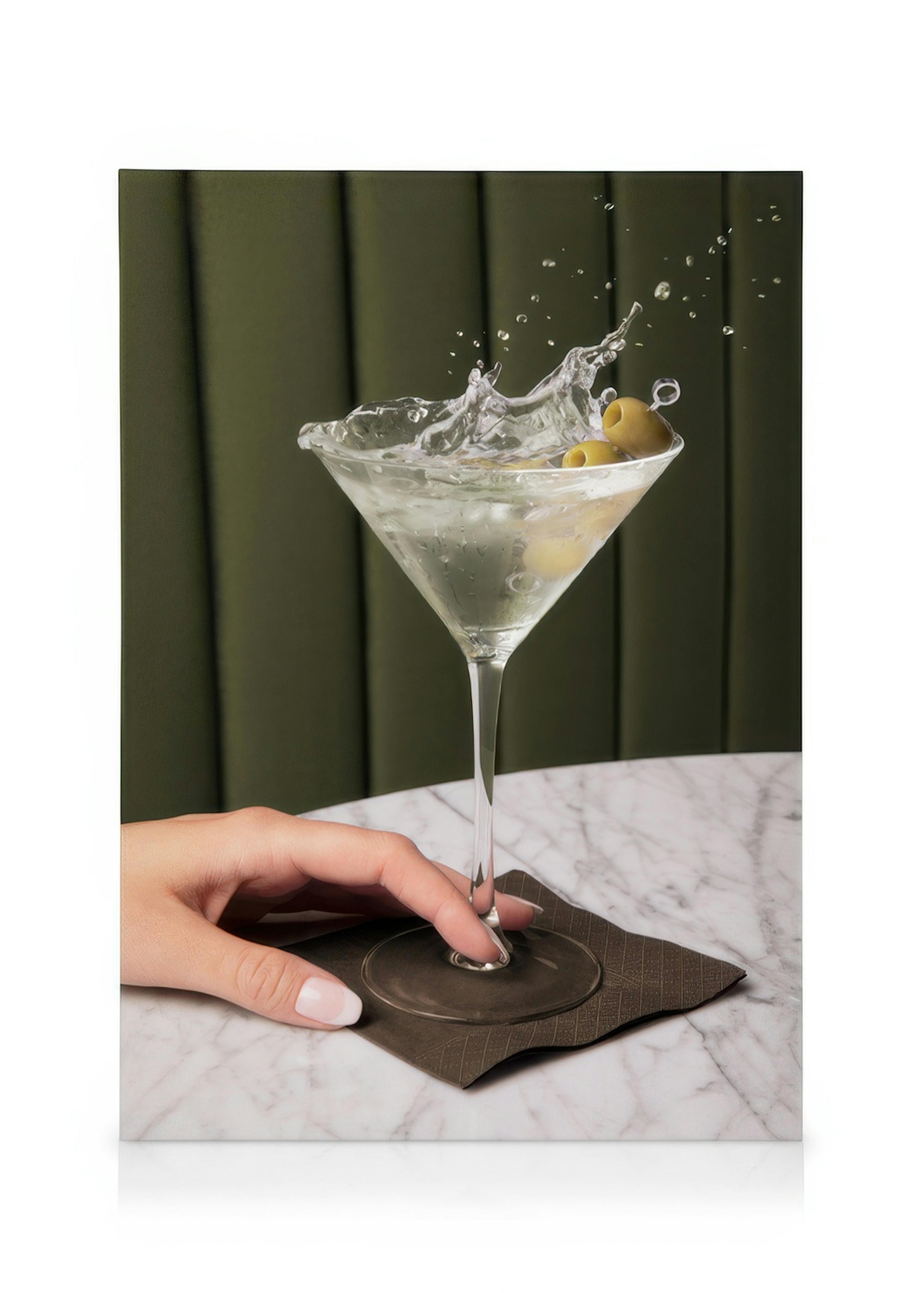 Hand holding a martini glass with splashing liquid and green olives against a green backdrop