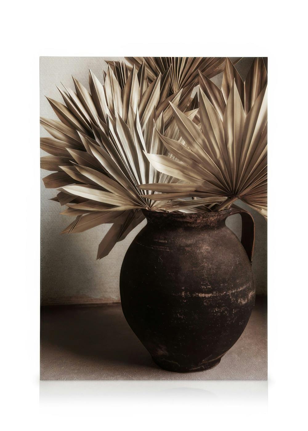 Rustika bruna palmblad i en brun lerkruka, med naturlig patina och neutrala toner. Klassisk konst.