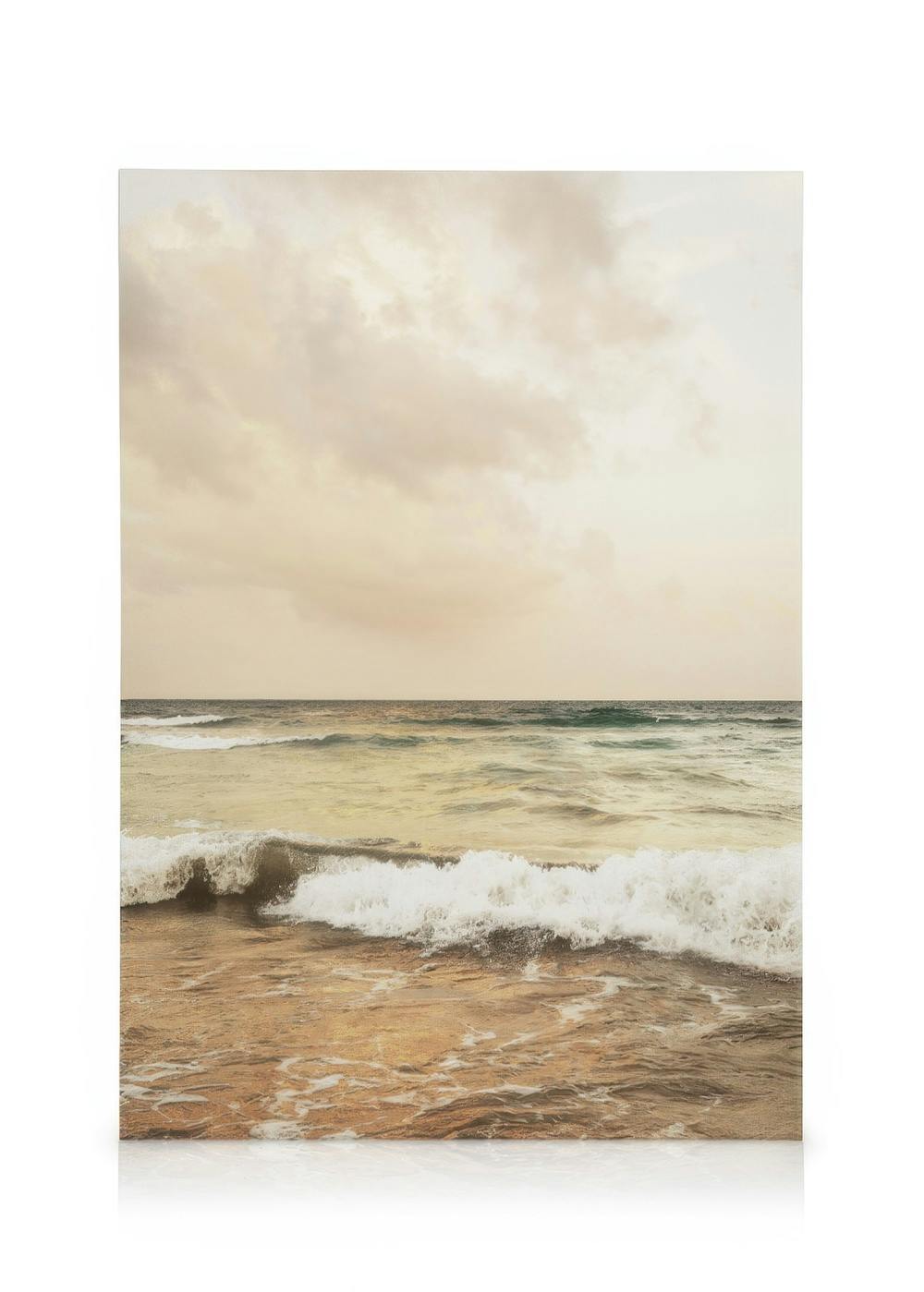 Toile de plage avec vagues sur le rivage, sable brun et ciel nuageux bleu, blanc et gris, évoquant un horizon marin.