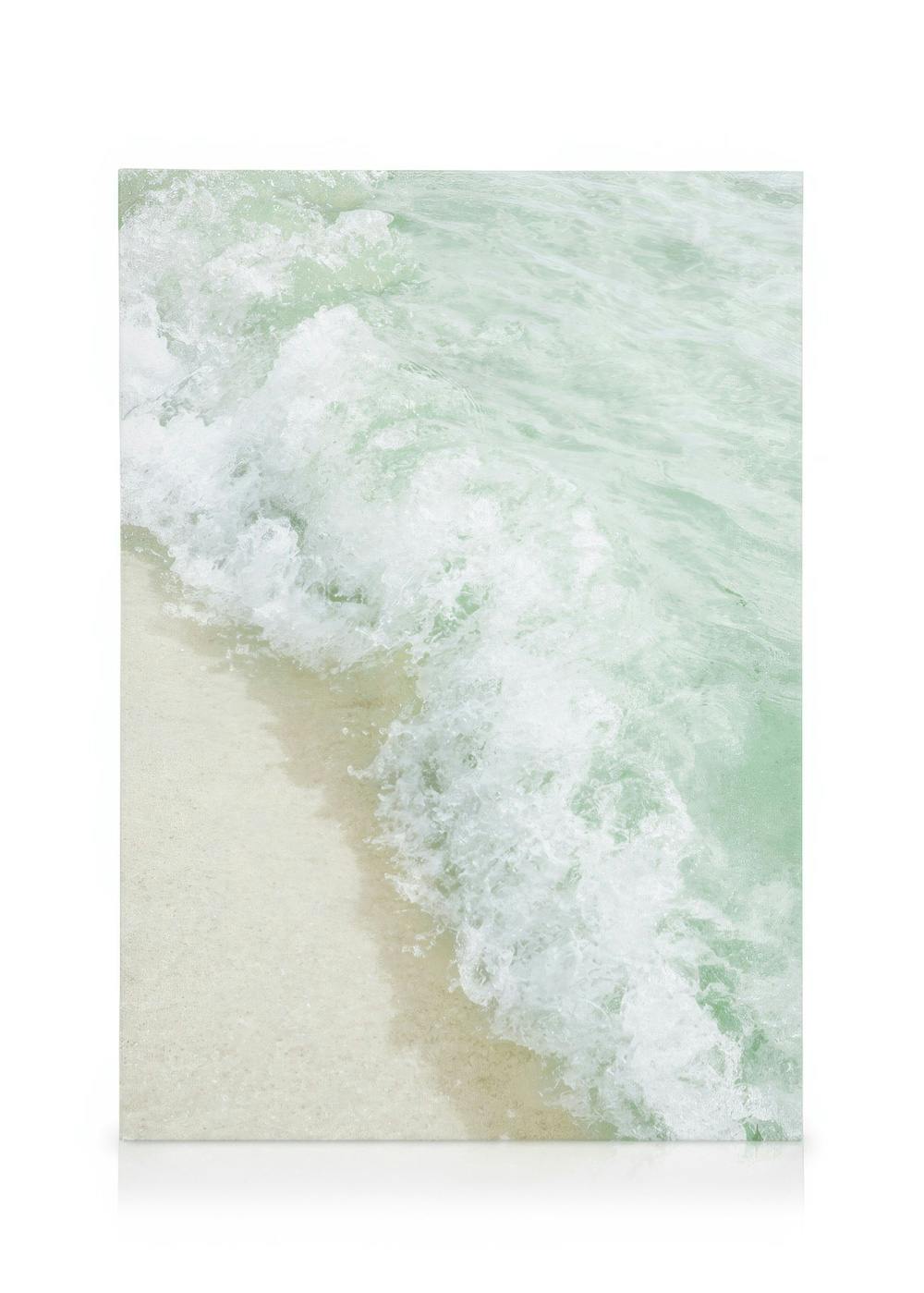 Toile de vague mousseuse verte et blanche sur plage de sable beige clair, ambiance douce et mer calme