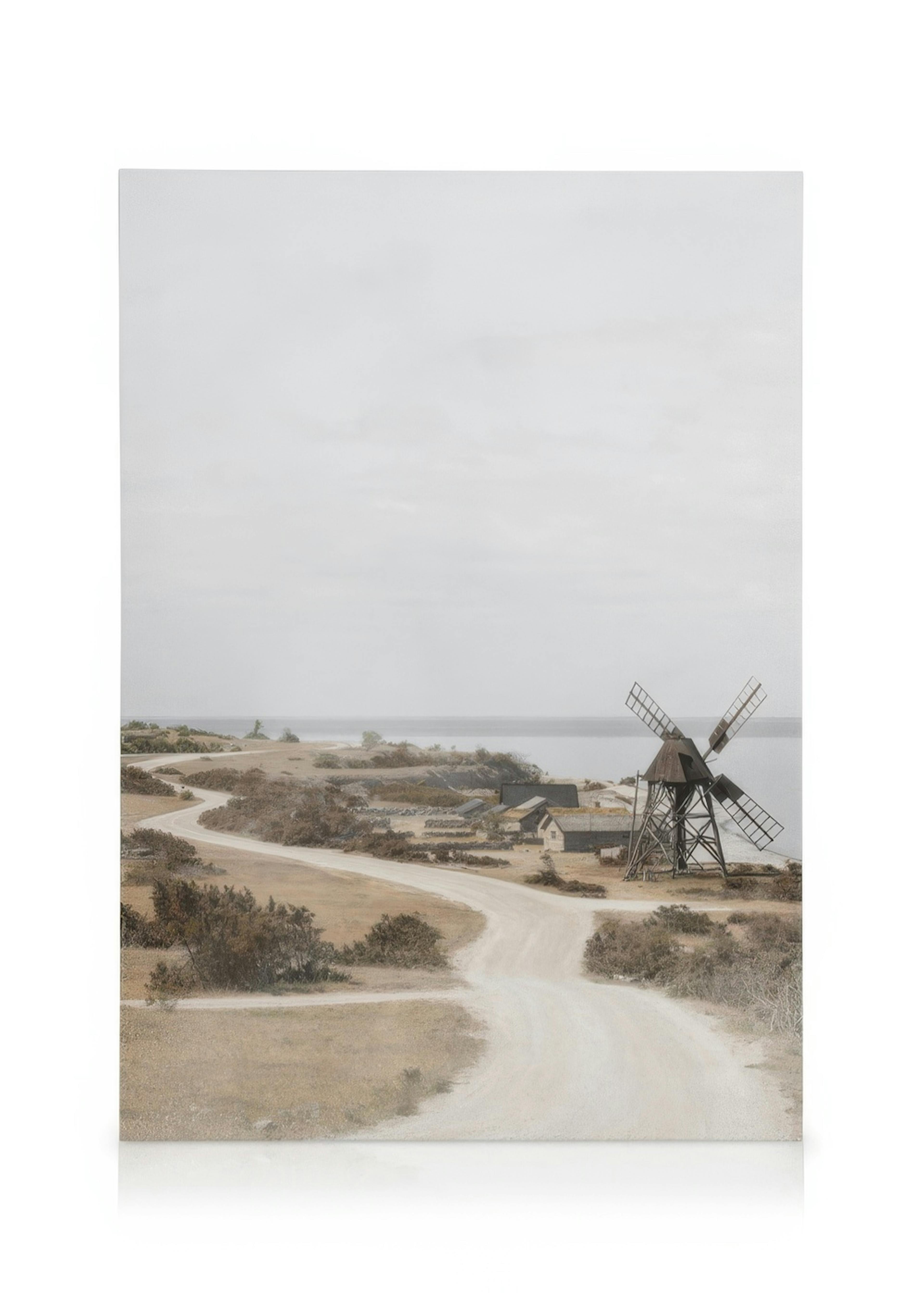 Ein gewundener Weg in einer kargen Küstenlandschaft mit einem alten Windrad und kleinen Häusern am Meer.
