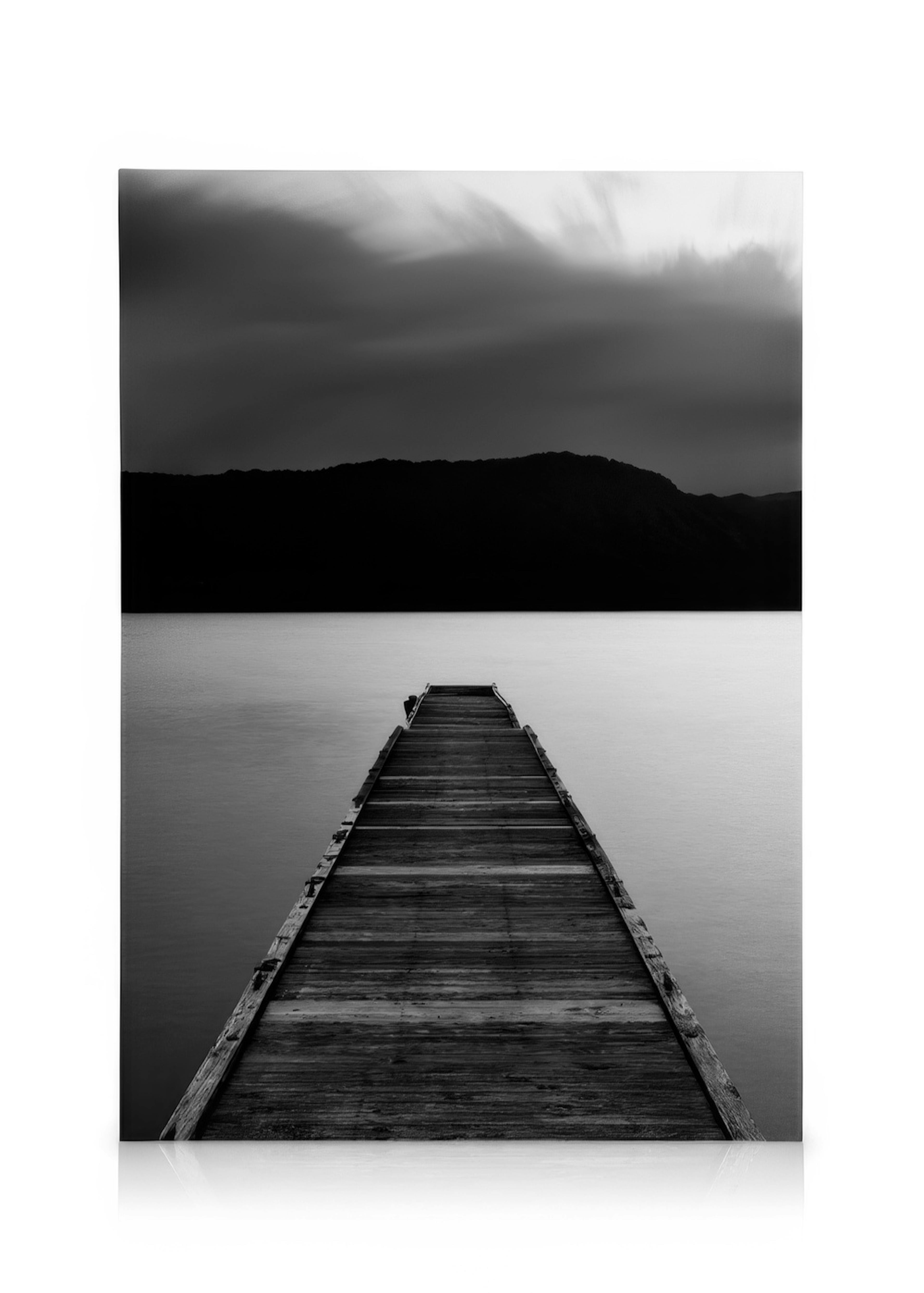 Quadro em tela de cais de madeira em preto e branco sobre lago calmo com montanhas e céu nublado.