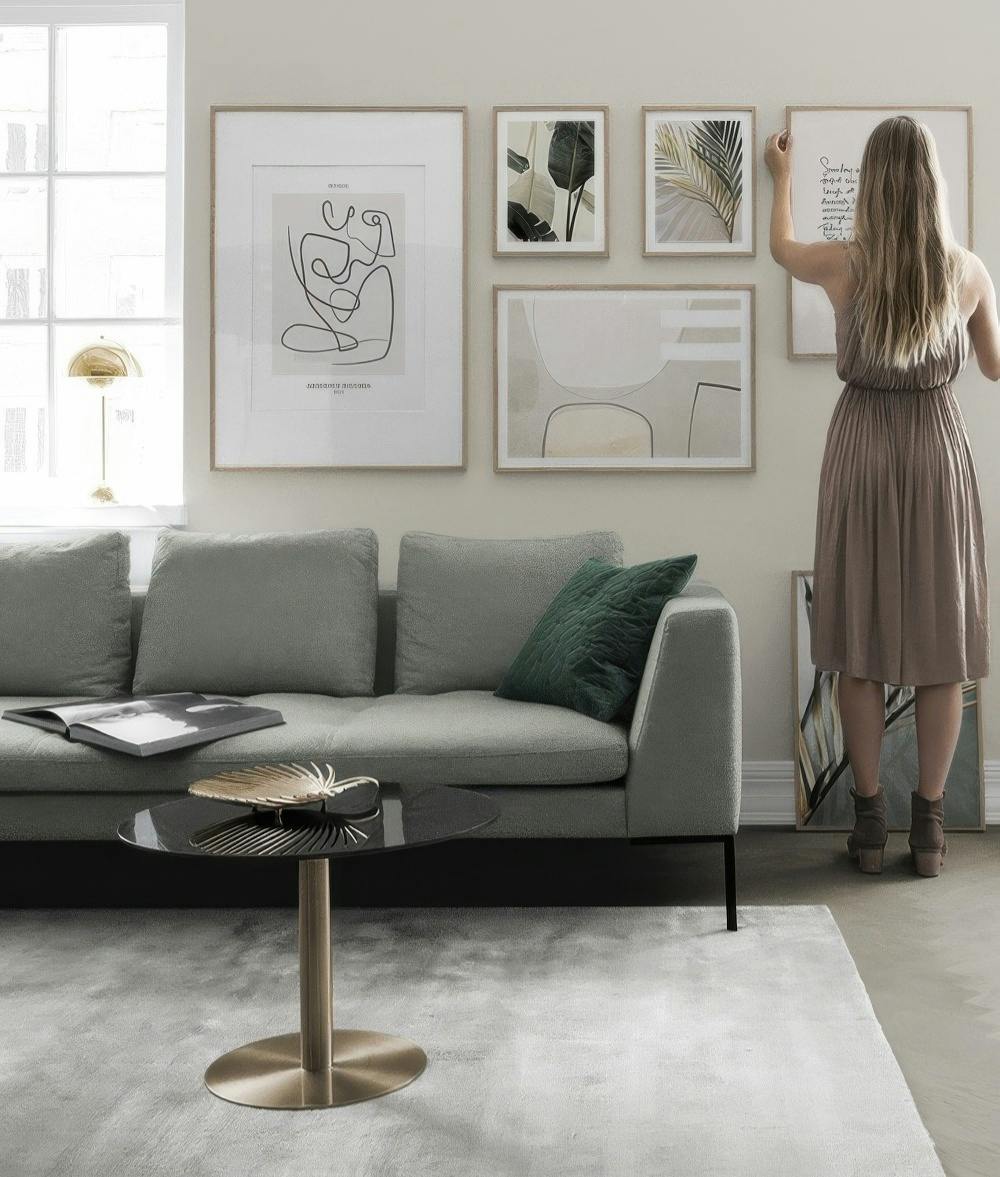 En tavelvägg med botaniska och abstrakta motiv i varma, jordnära färger över en soffa i ett vardagsrum.