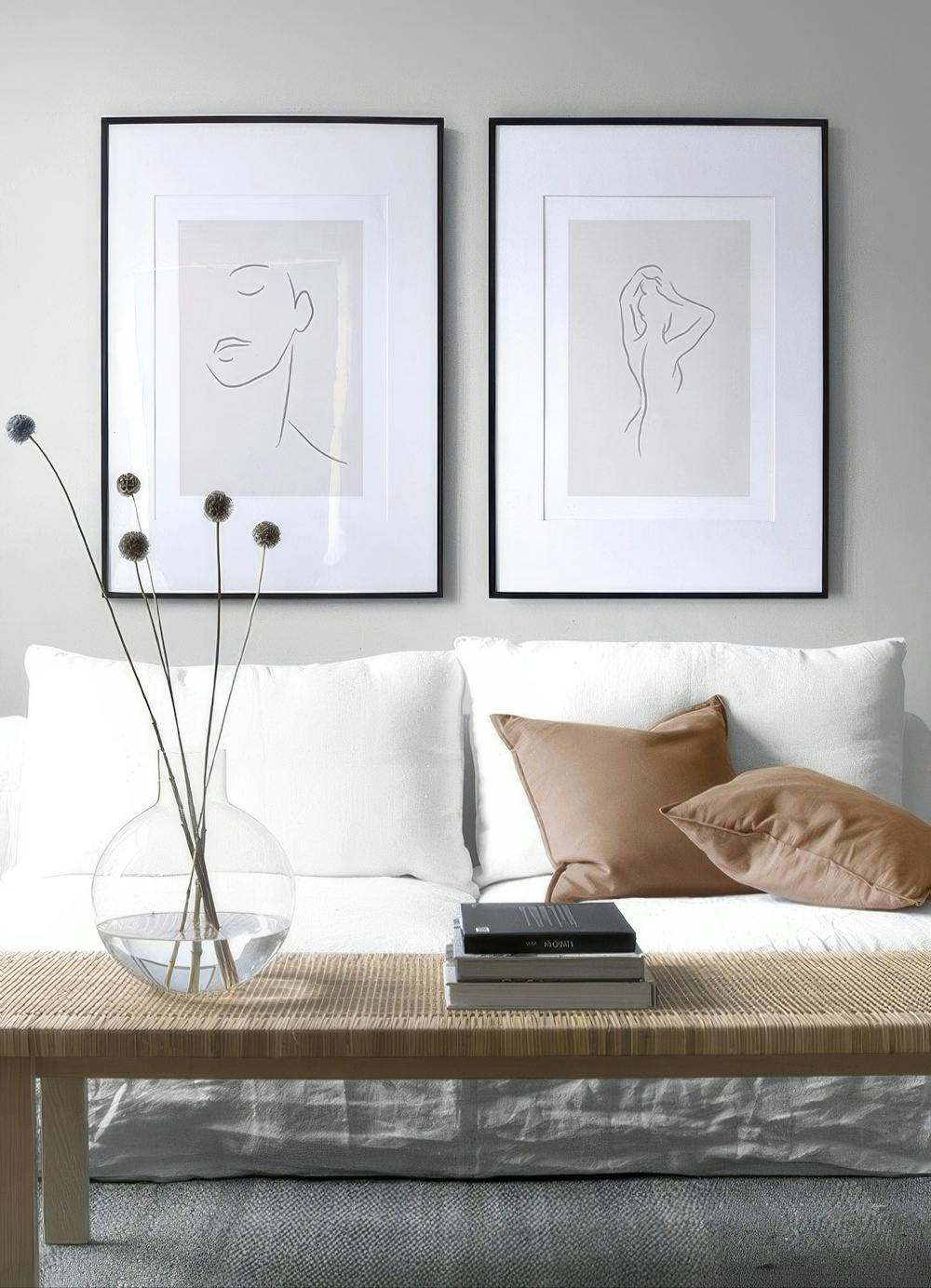 Galleria a parete con due stampe artistiche minimaliste di figure umane delineate su sfondo chiaro, sopra un divano bianco.