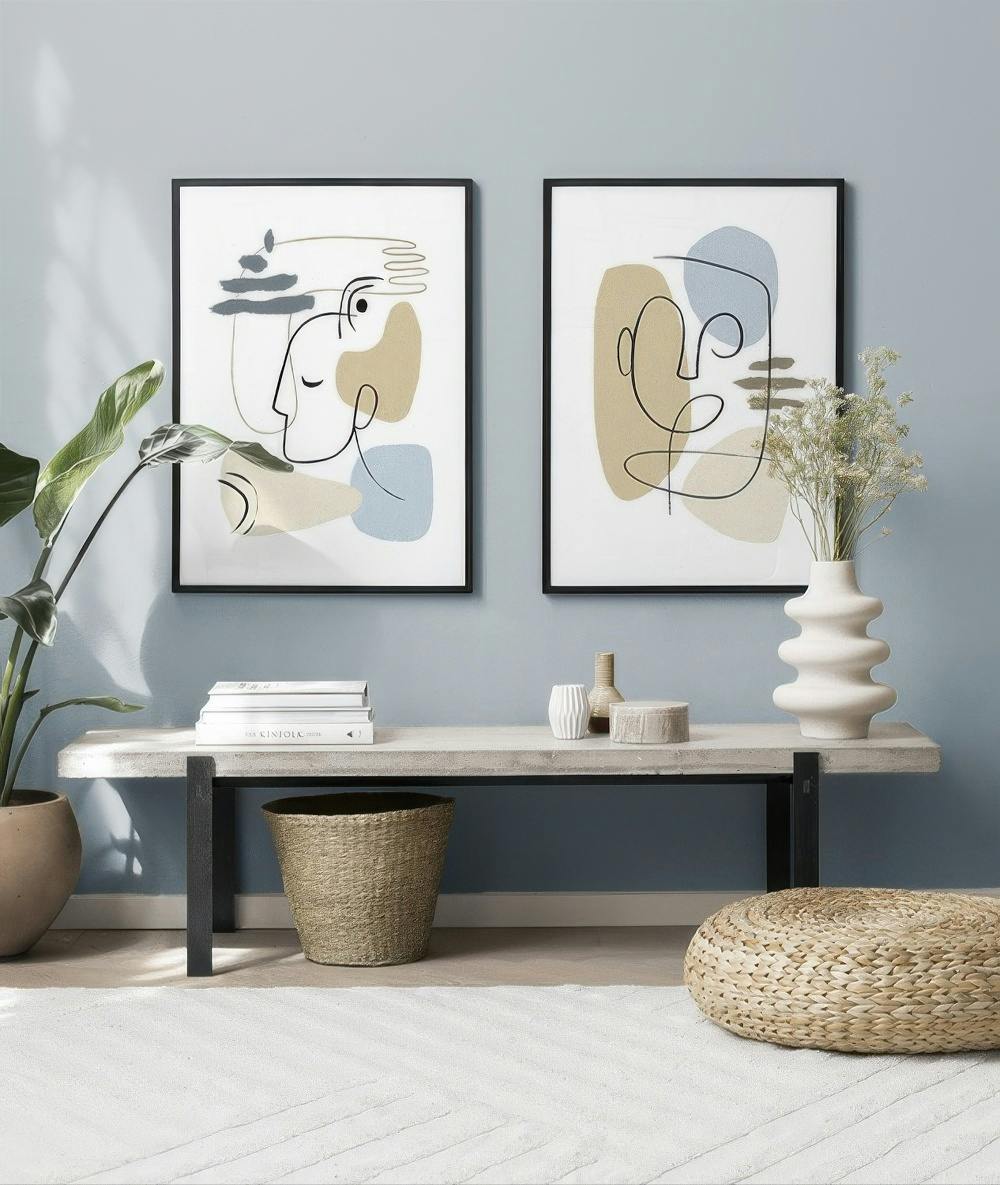Décoration murale de deux affiches abstraites aux visages esquissés, formes beige et bleu pâle sur un mur bleu.