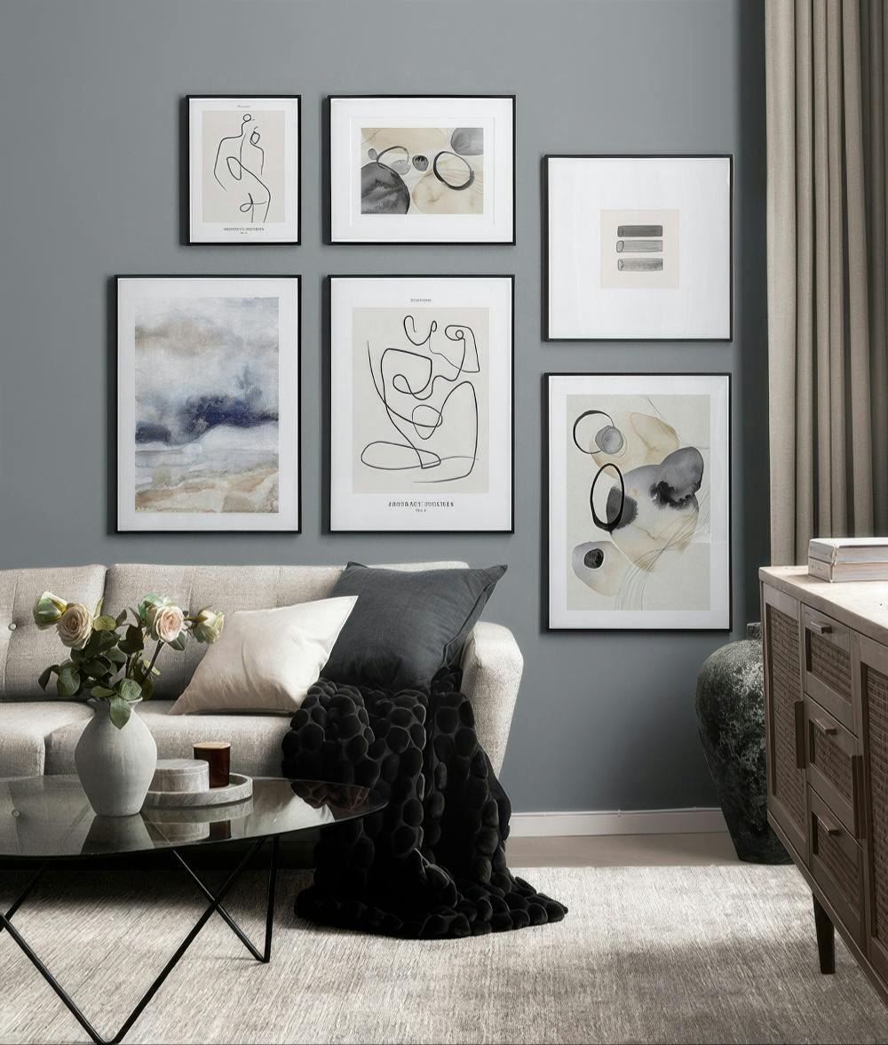 Een galeriewand met abstracte prints in grijze, beige en zwarte tinten, met organische vormen en lijnen, boven een bank.